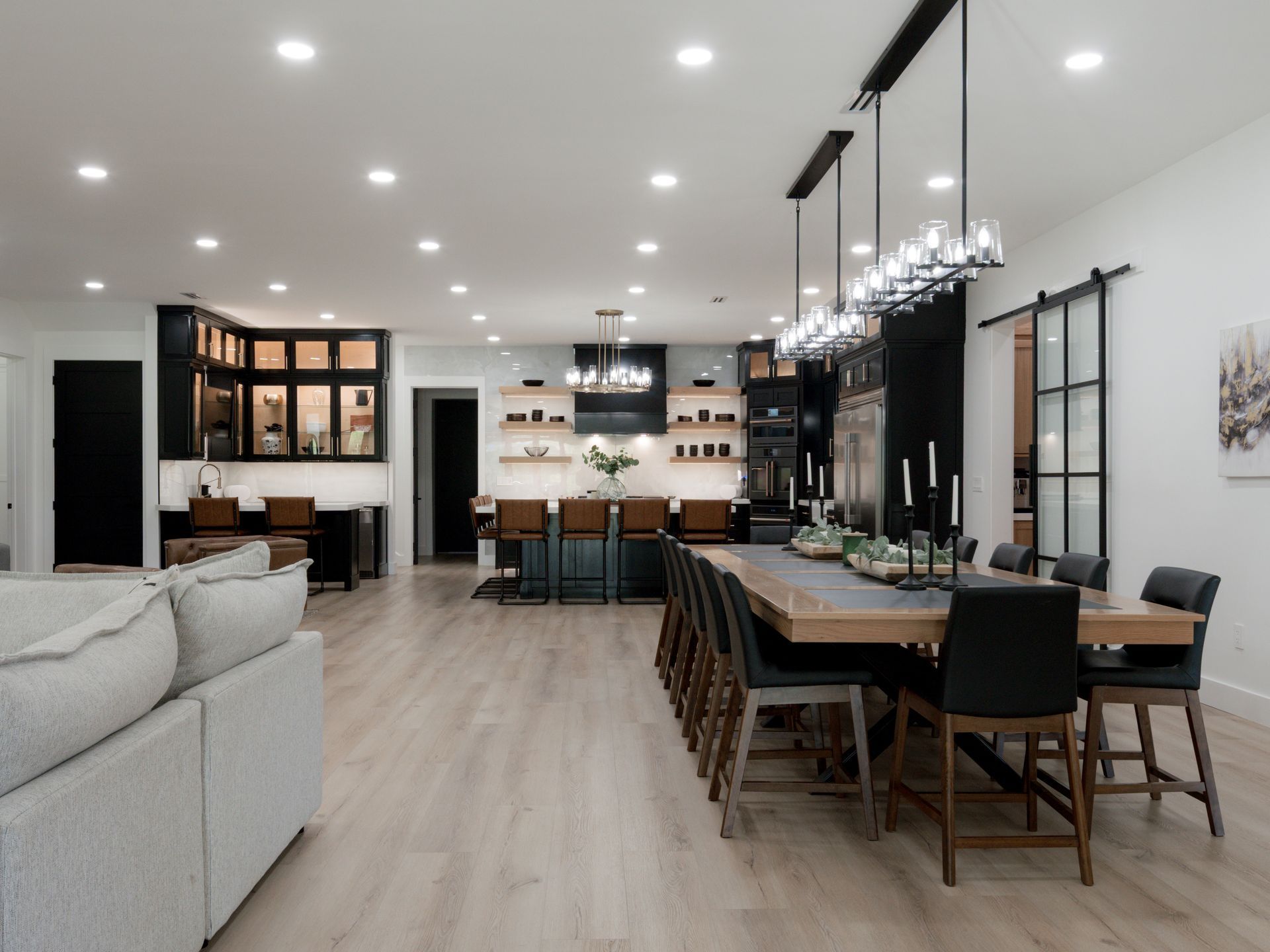 Bright open-concept living and dining room with long table, sofa, and modern kitchen lights