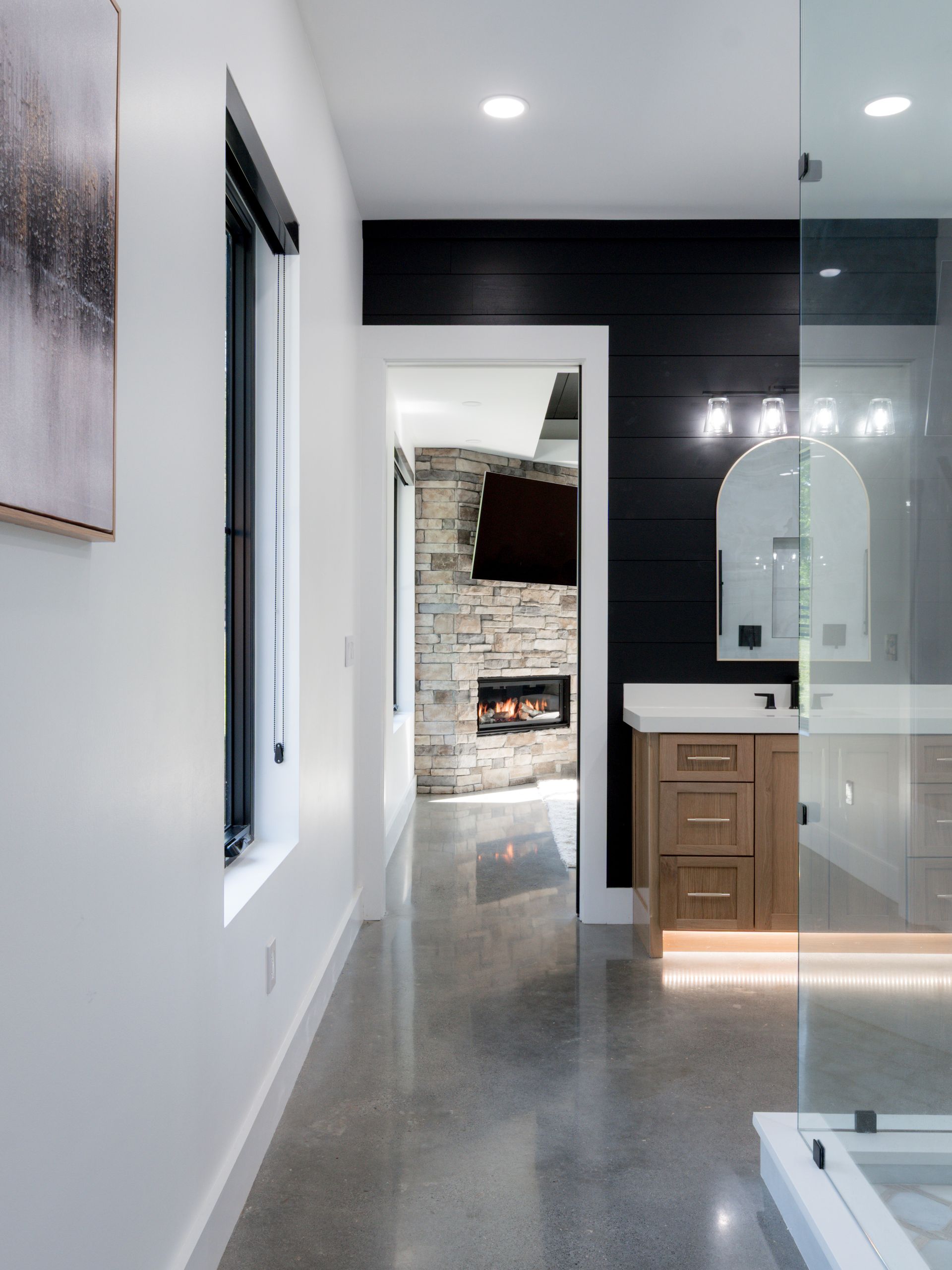 Modern bathroom with glass shower, wooden vanity, and open doorway to a stone patio.