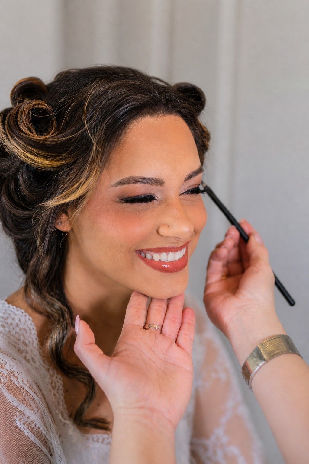 Woman having eye makeup applied while smiling; close-up beauty scene with a makeup brush.