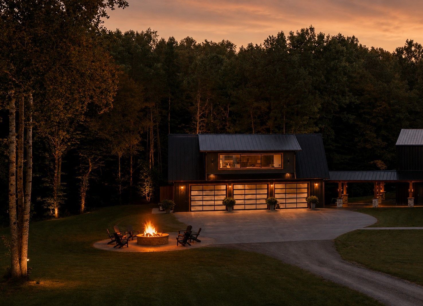 Cabin with warm lights at dusk, people around a campfire in a wooded clearing.