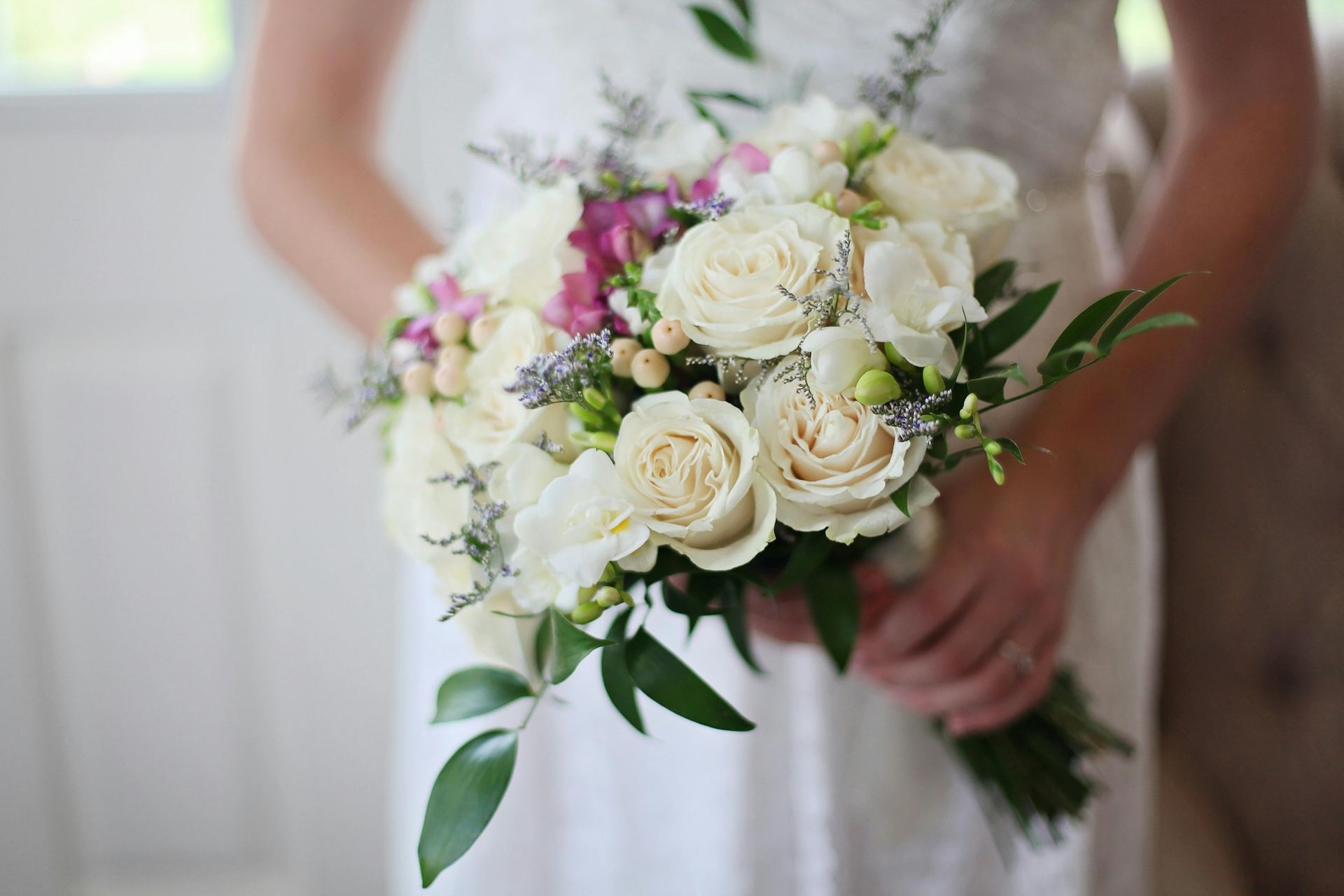 Bride holding a white and blush bouquet with greenery, wearing a white dress