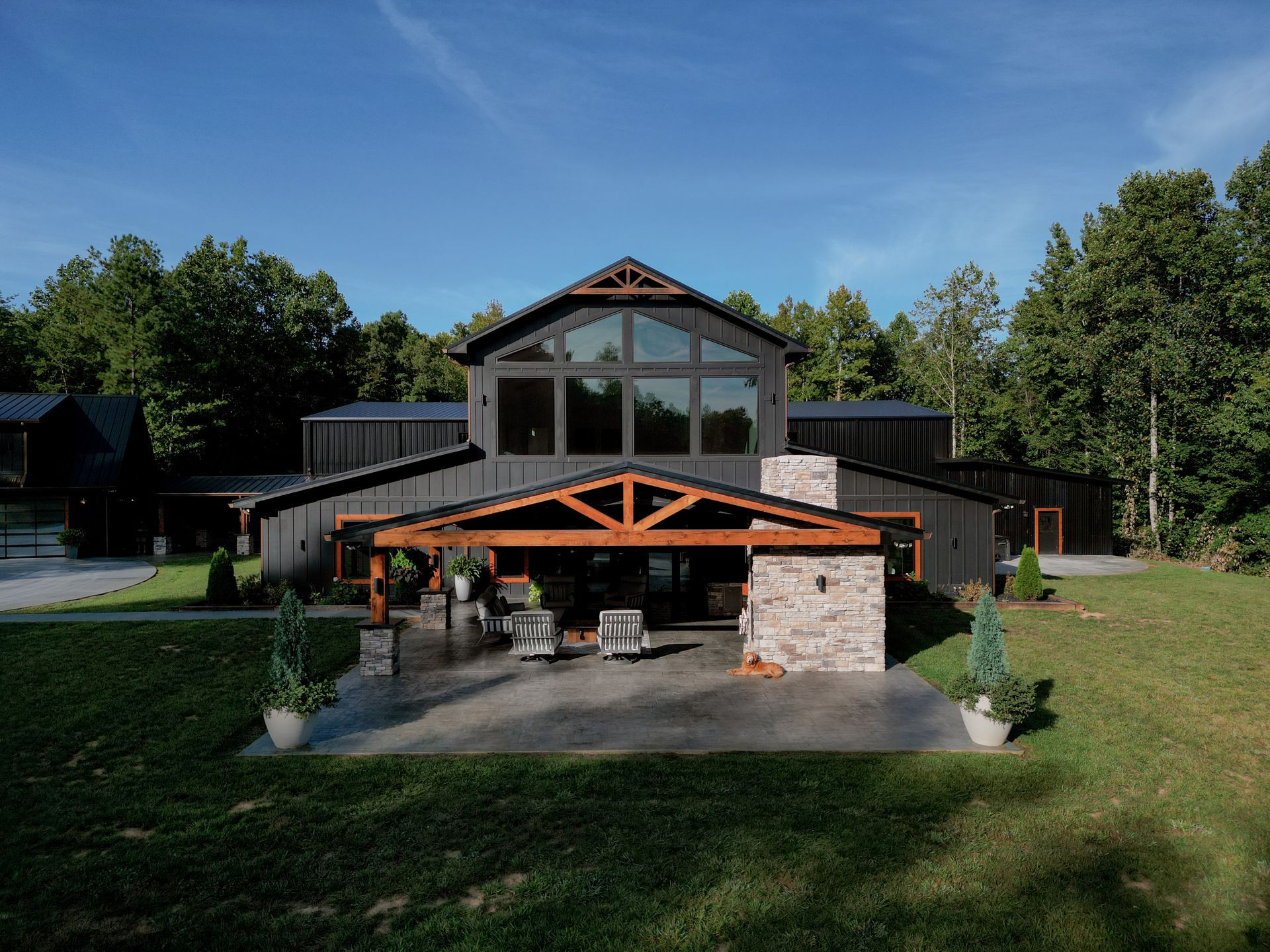 Modern house with large windows, wooden patio, and stone foundation in a grassy yard under a blue sky