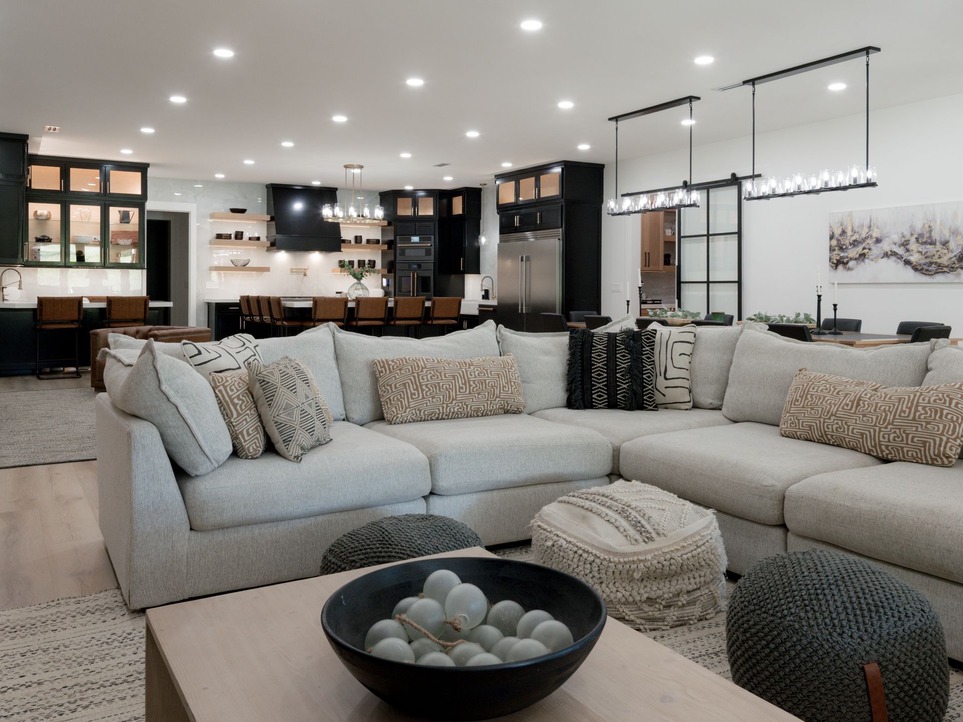 Modern open-concept living room with a light sectional sofa, coffee table, and kitchen in the background