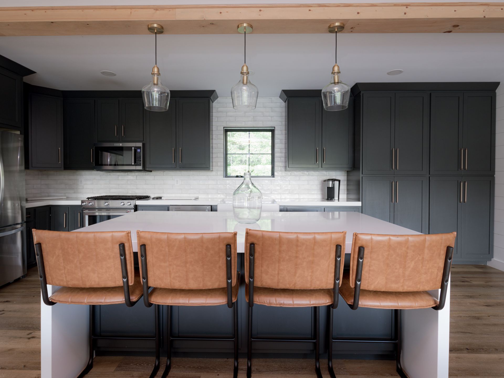 Modern kitchen with dark cabinets, white island, and four tan bar stools under pendant lights