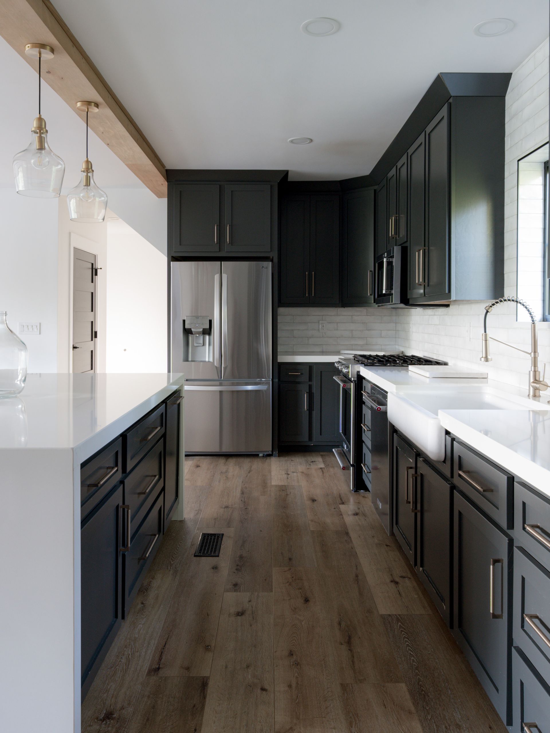 Modern kitchen with black cabinets, stainless steel appliances, white countertops, and wood flooring