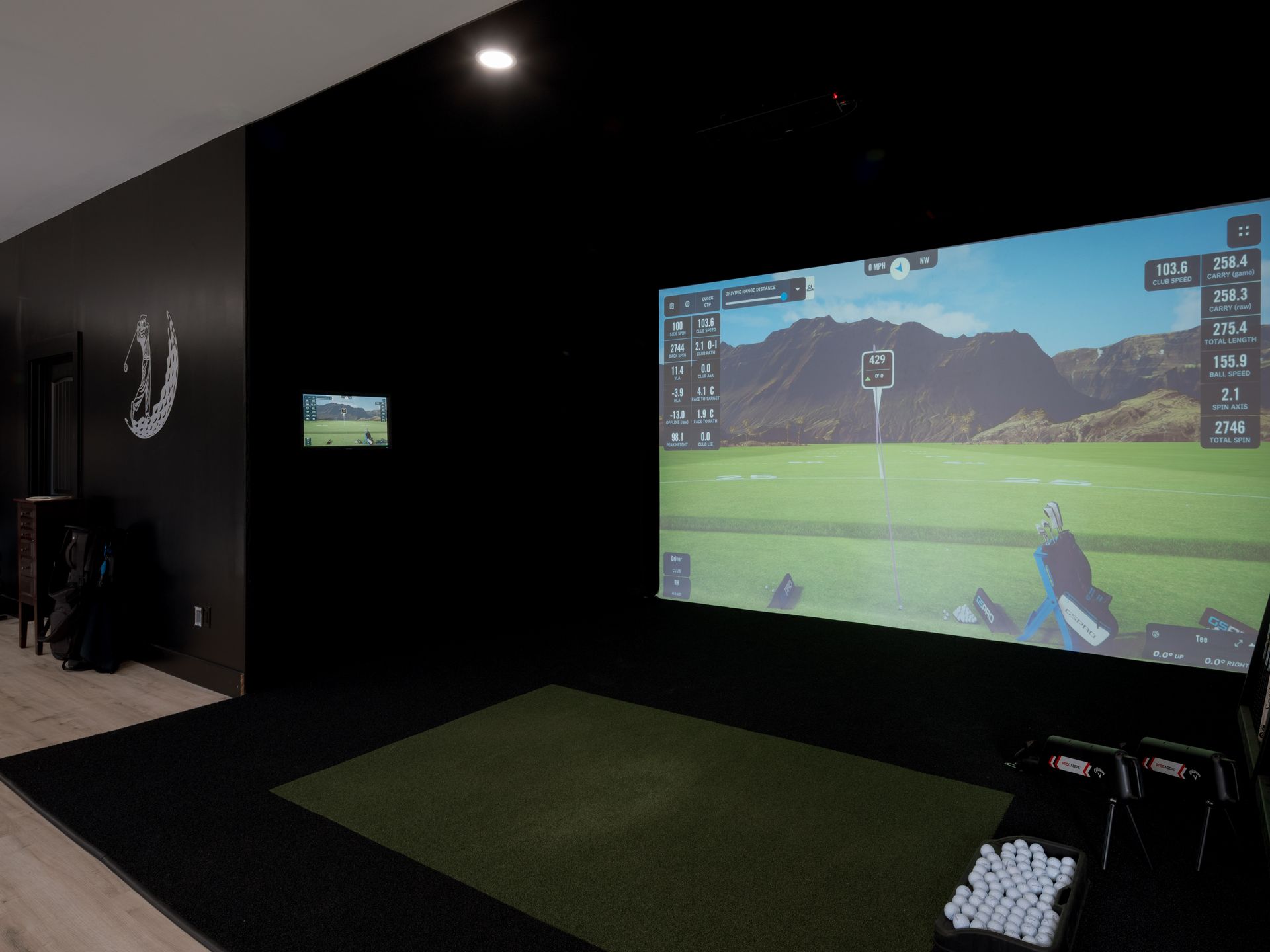 Indoor golf simulator room with projected golf course, turf mat, and black walls