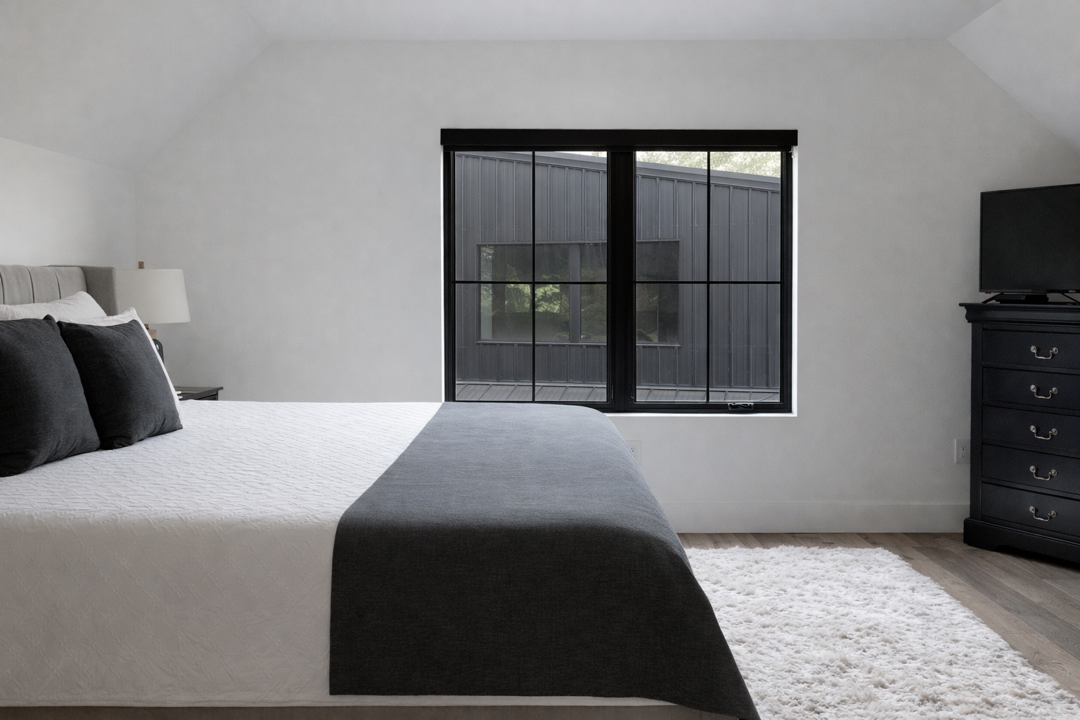 Minimalist bedroom with gray bed, black window, white rug, and dark dresser