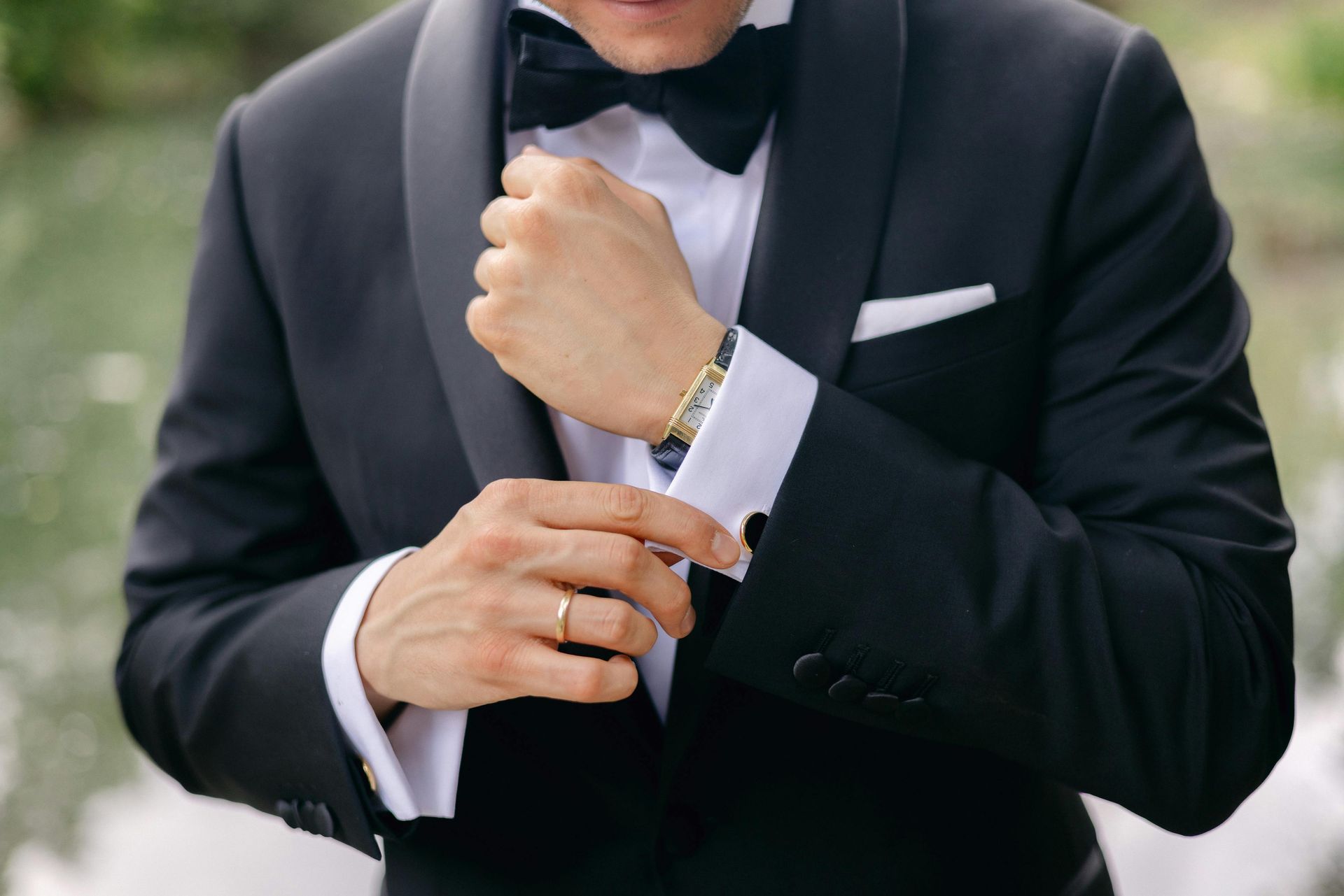 Man in a black tuxedo adjusting his cuff and jacket before a formal event