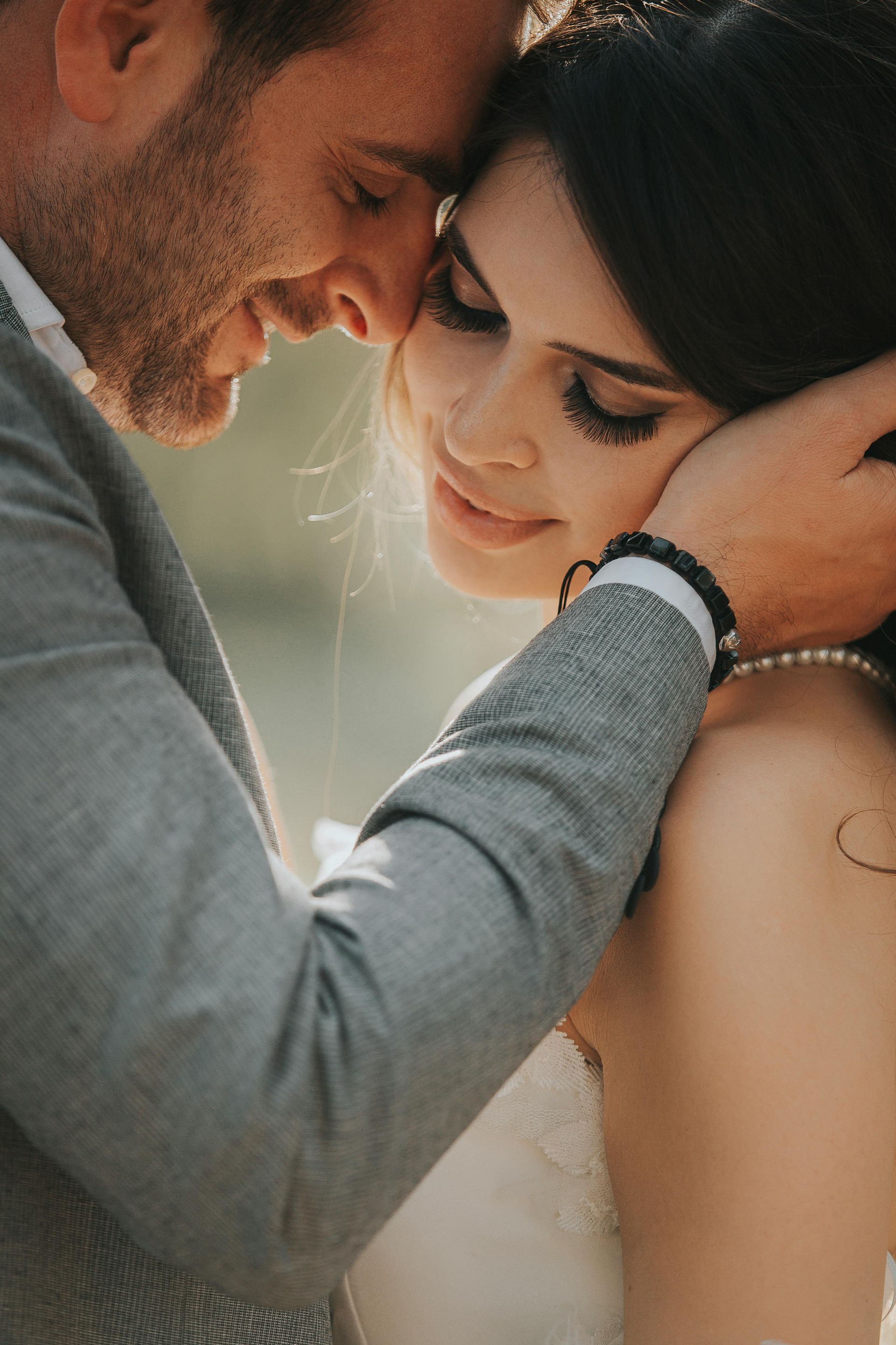 Couple embracing closely outdoors, foreheads touching in soft natural light.