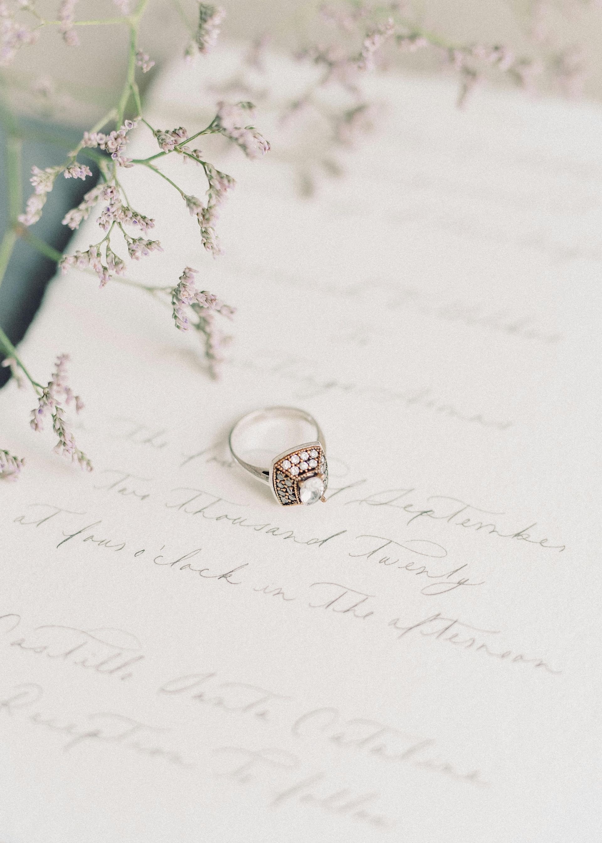 Pearl ring on handwritten paper beside delicate flowers, in soft pastel tones