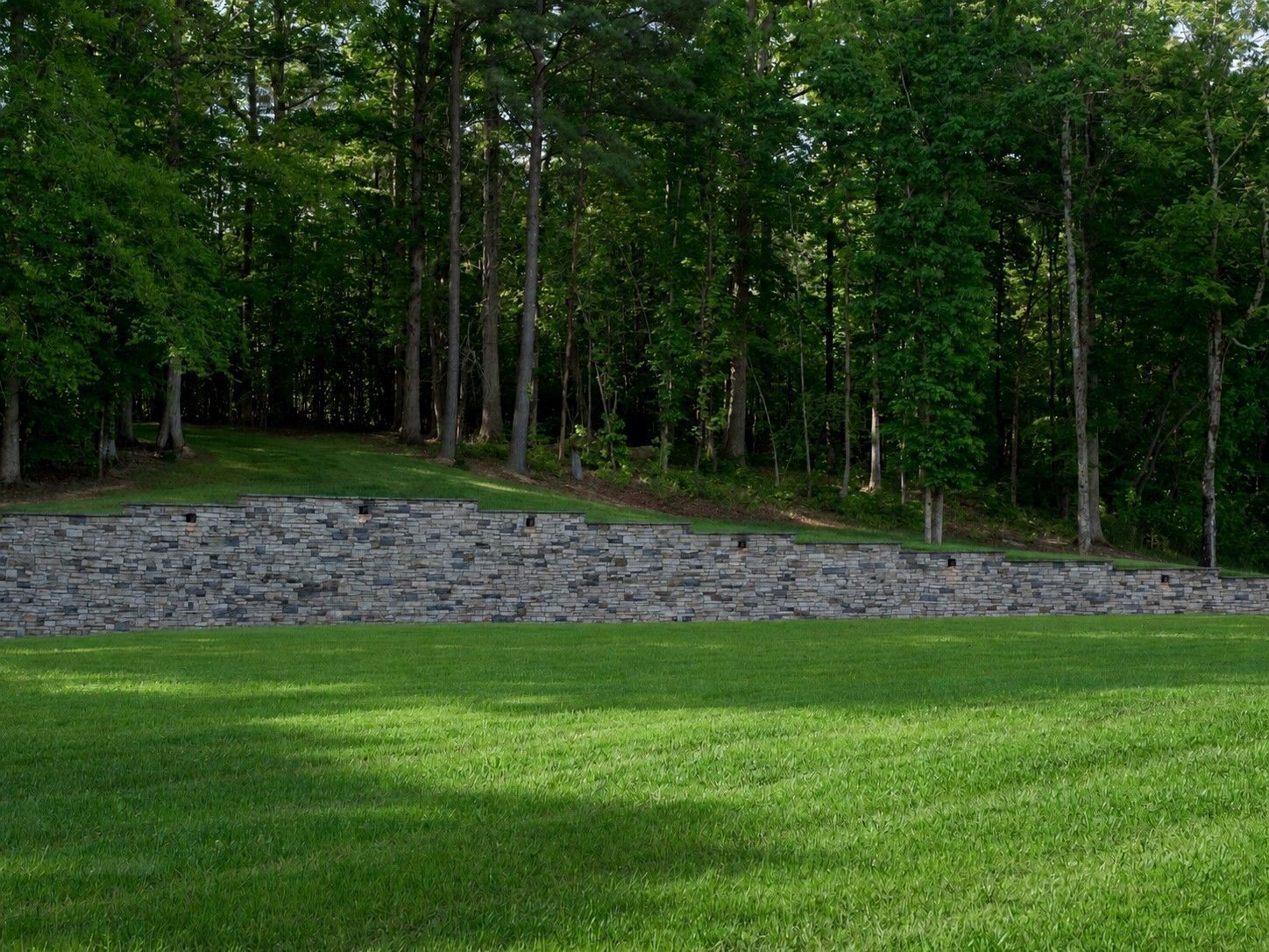 Grassy foreground with a wooded backdrop and a gray stone embankment