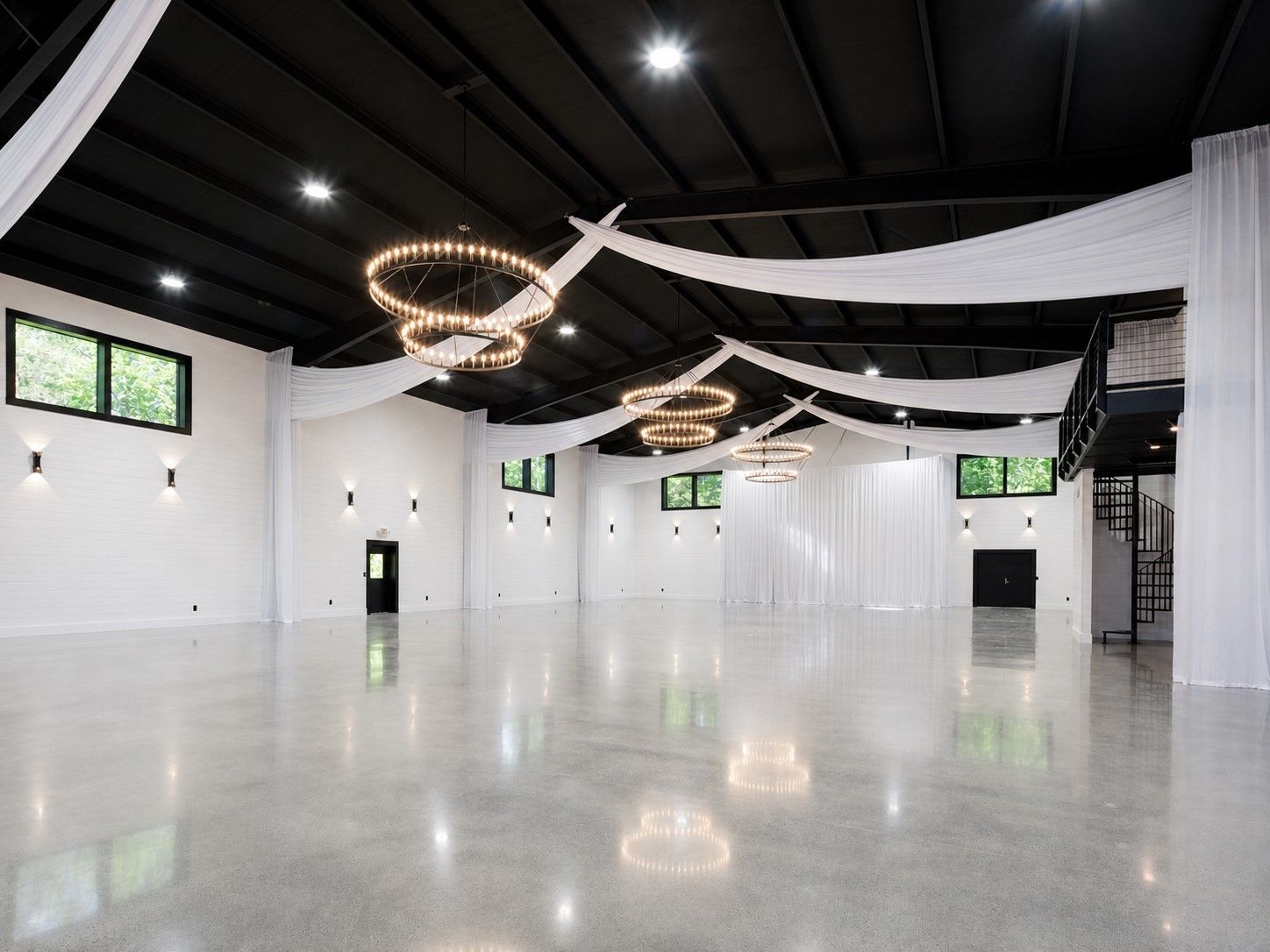 Elegant banquet hall with round tables, black chairs, white linens, and modern chandeliers under draped black ceiling fabric