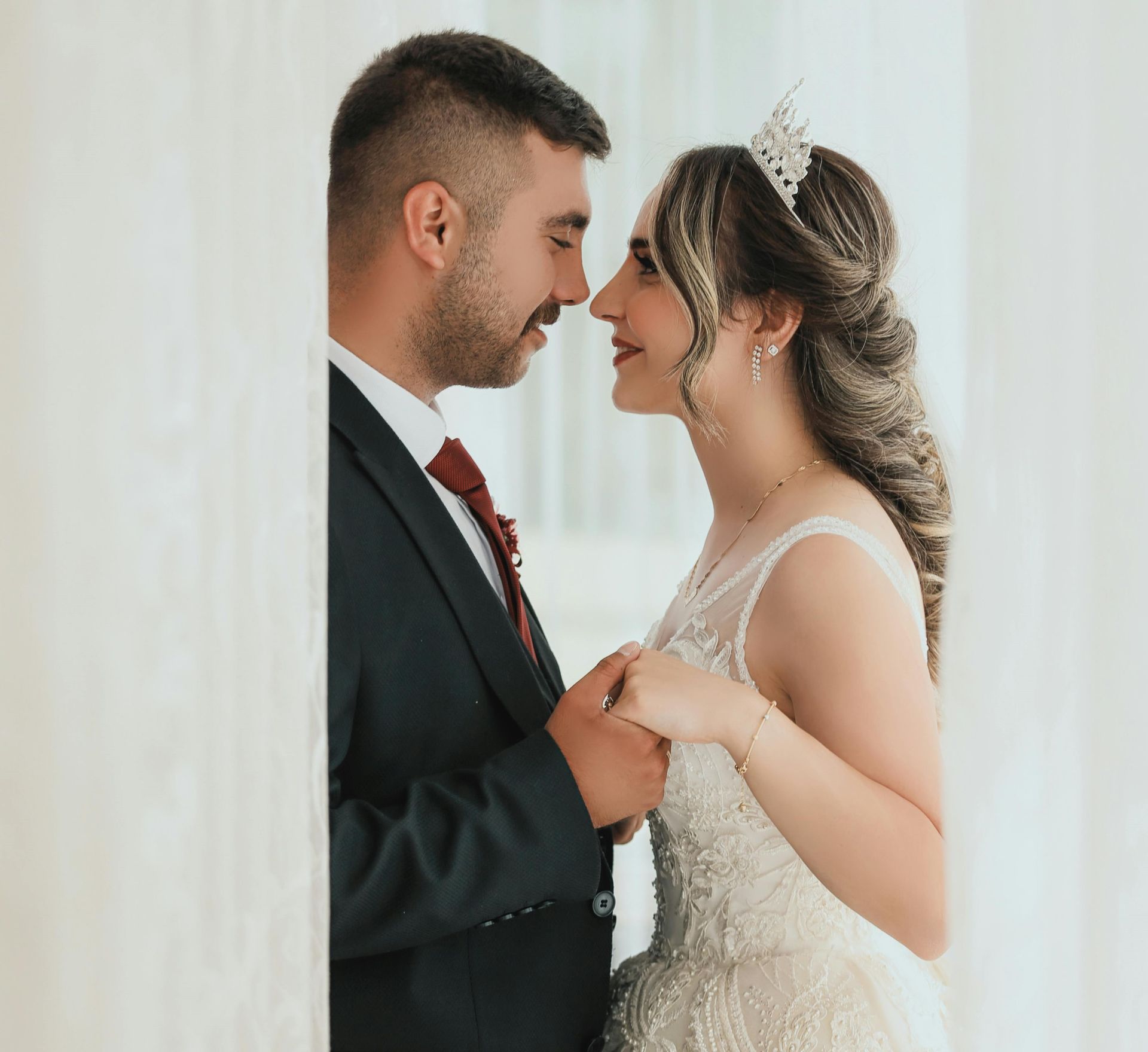 Bride and groom hold hands and smile face-to-face in a bright wedding setting