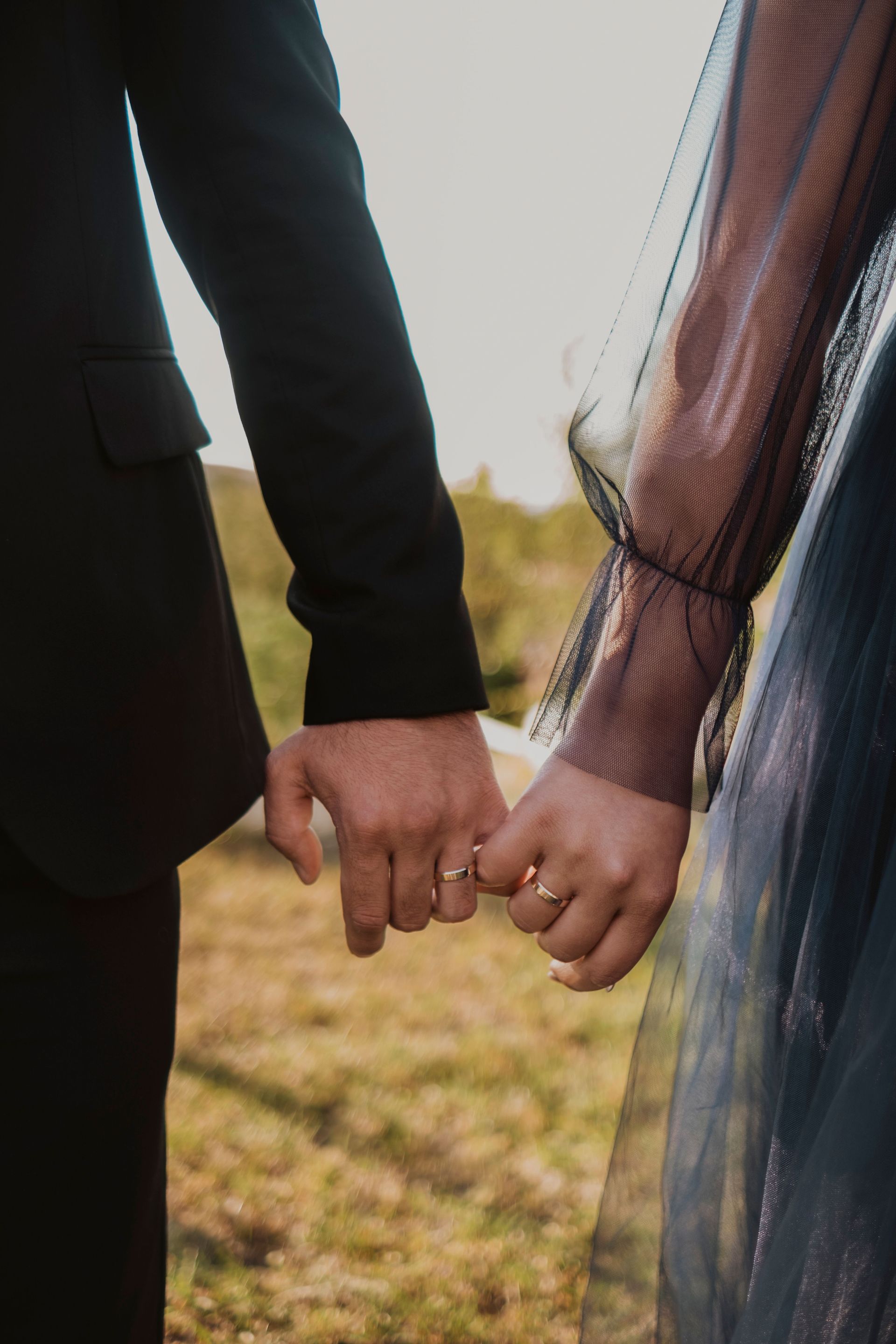 Two people holding hands outdoors, one in black sleeves and the other in a sheer dark blue top.
