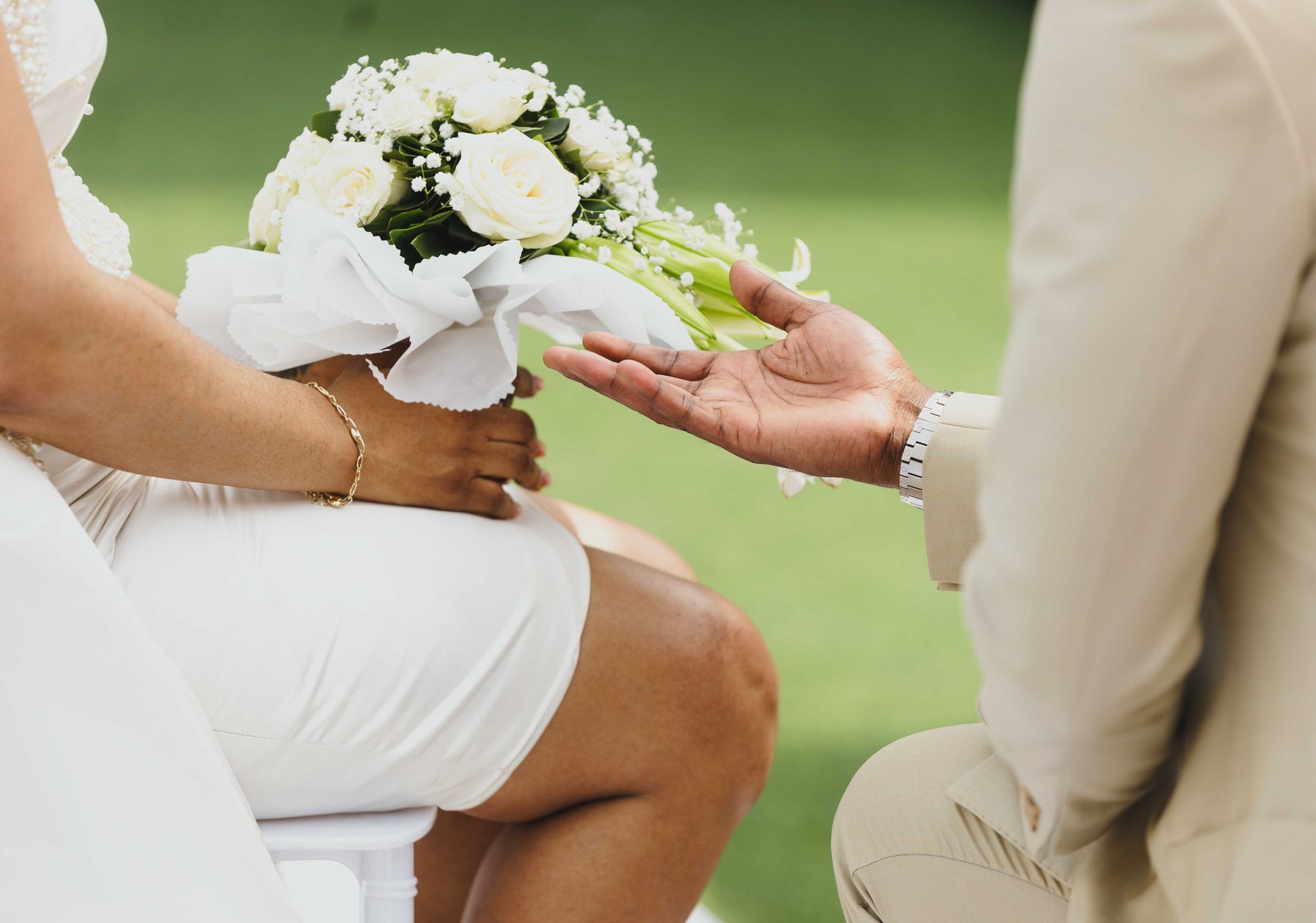 Hands holding a white bridal bouquet at an outdoor wedding ceremony