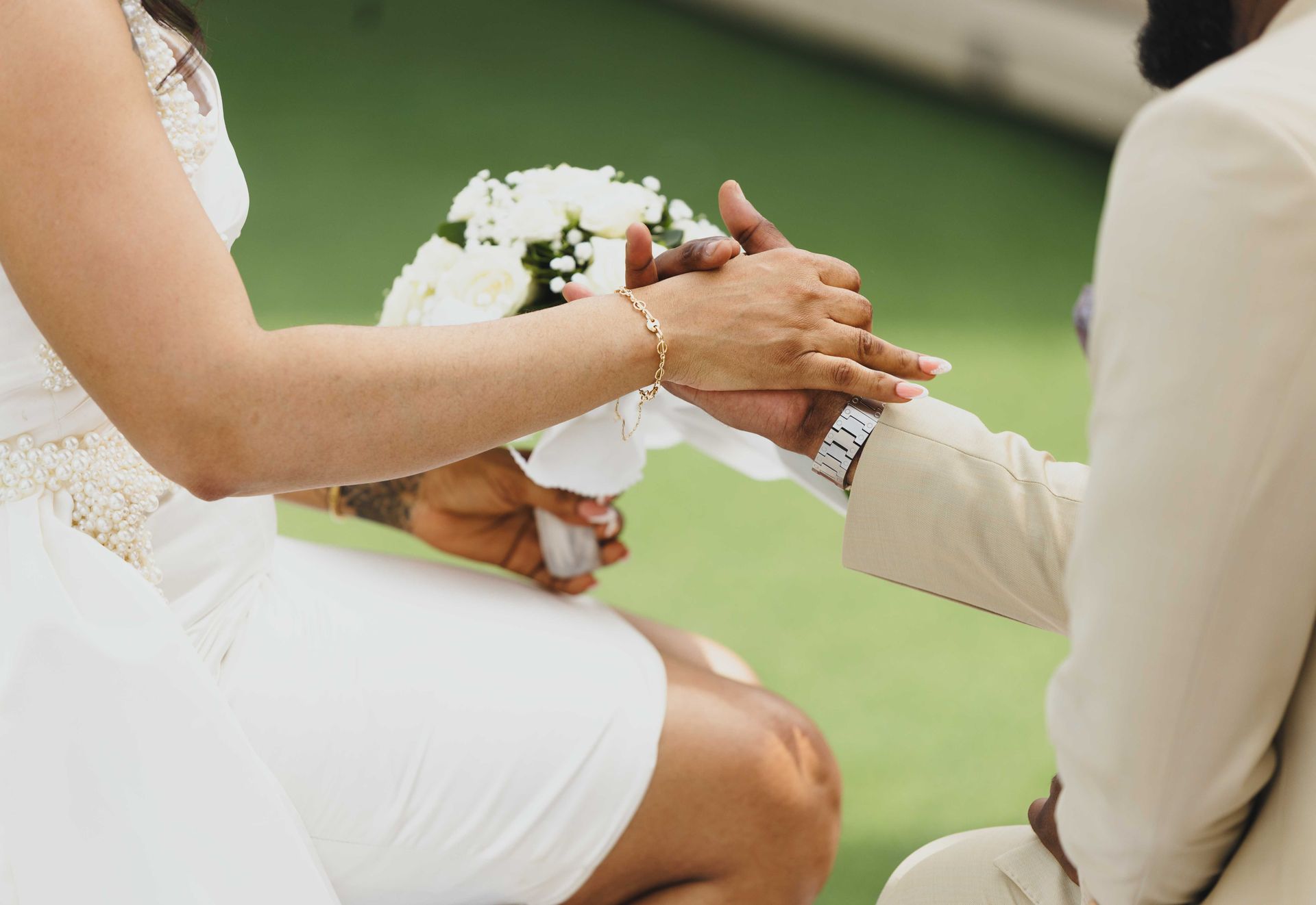 Two people exchanging wedding rings at an outdoor ceremony, with a bride in white and groom in beige.