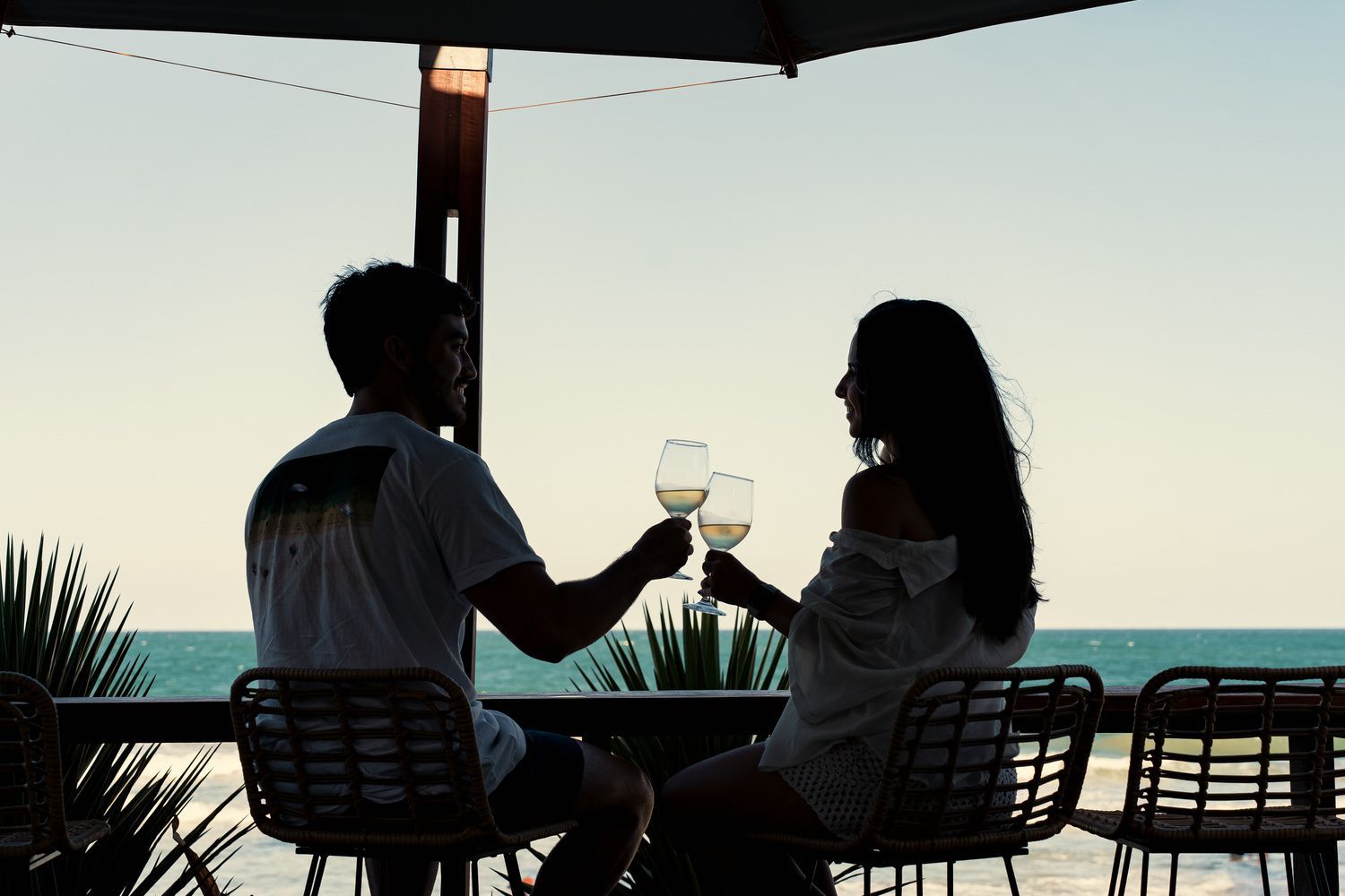 Um homem e uma mulher estão sentados à mesa brindando com taças de vinho.