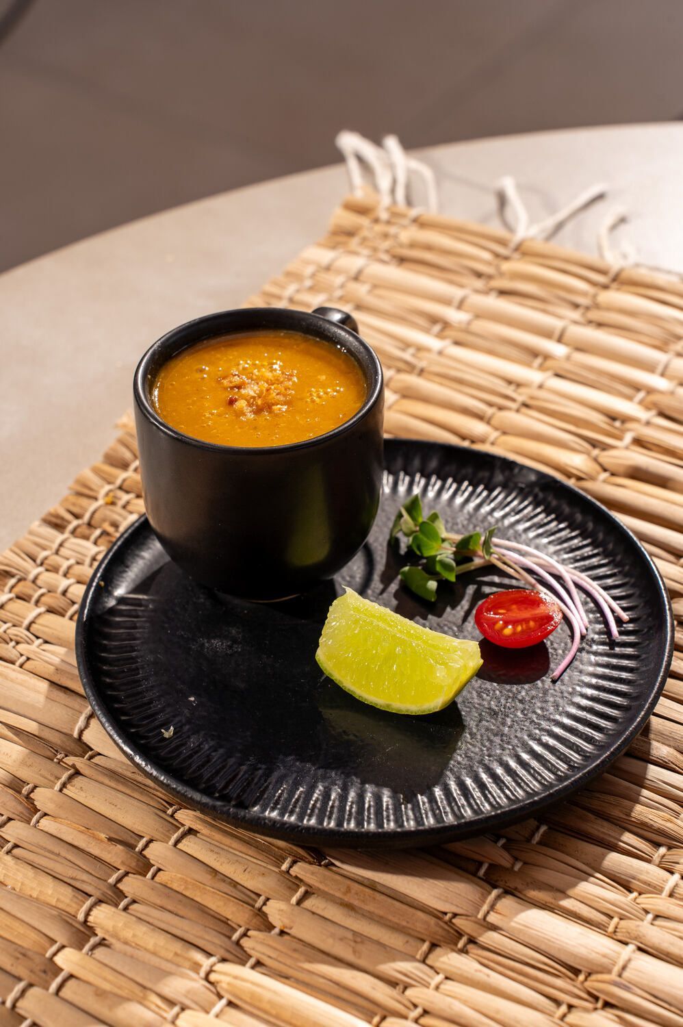 Uma xícara de sopa está sobre um prato preto sobre uma mesa.