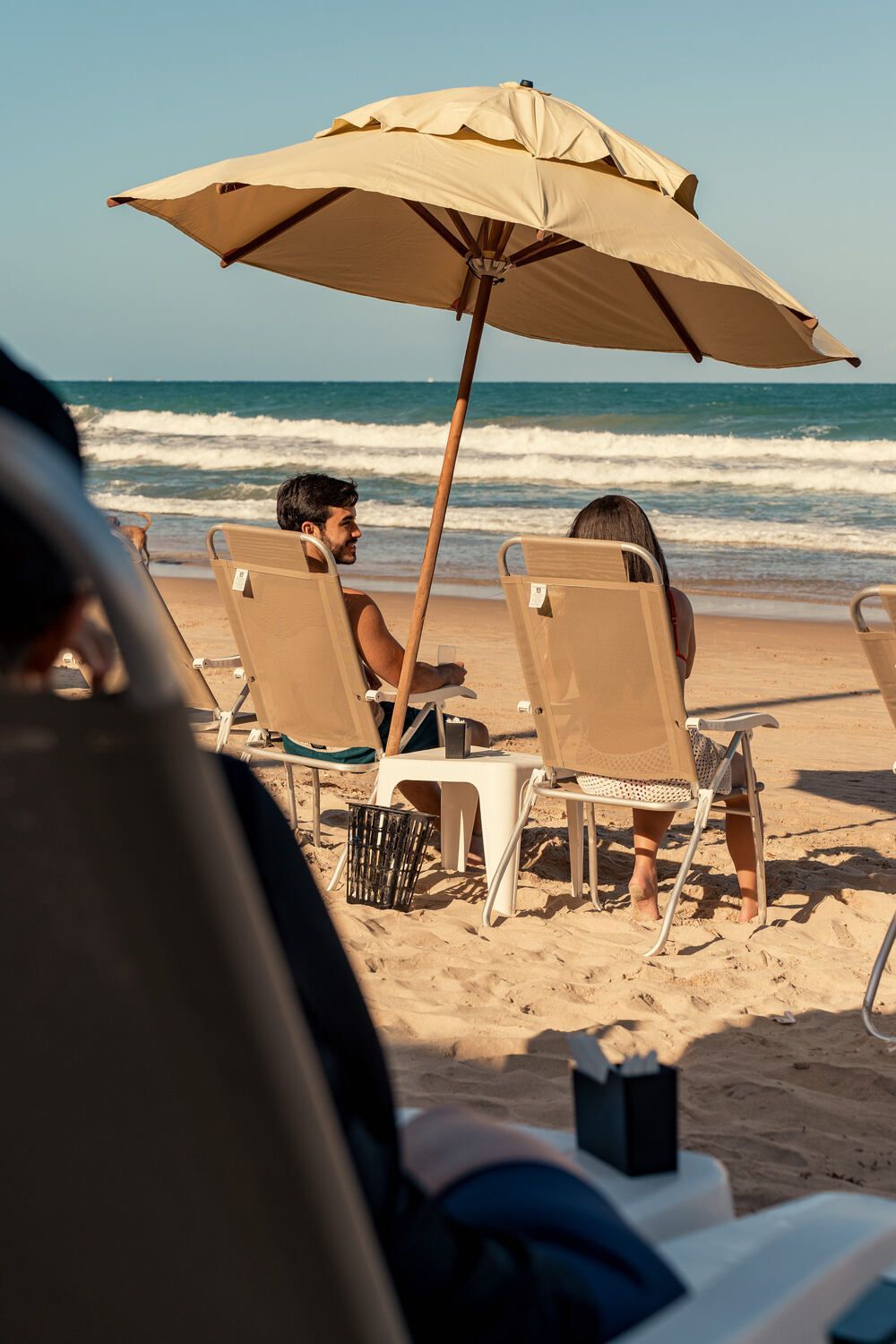 Um homem e uma mulher estão sentados sob um guarda-sol na praia.