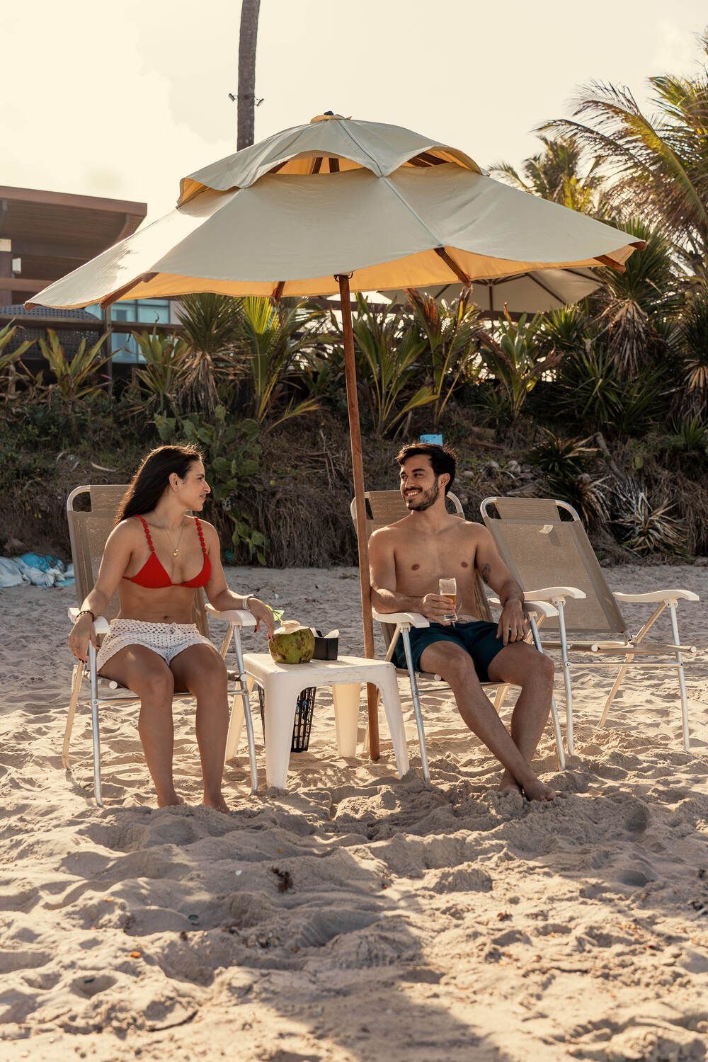 Um homem e uma mulher estão sentados sob um guarda-sol na praia.