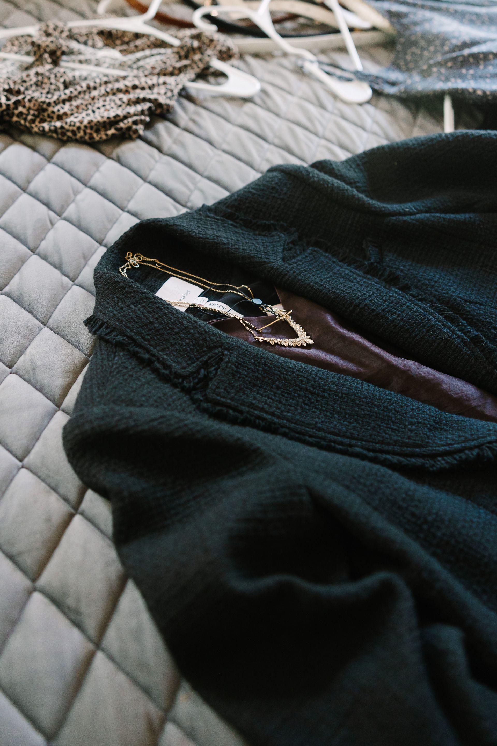 A black jacket is laying on top of a quilt on a bed.
