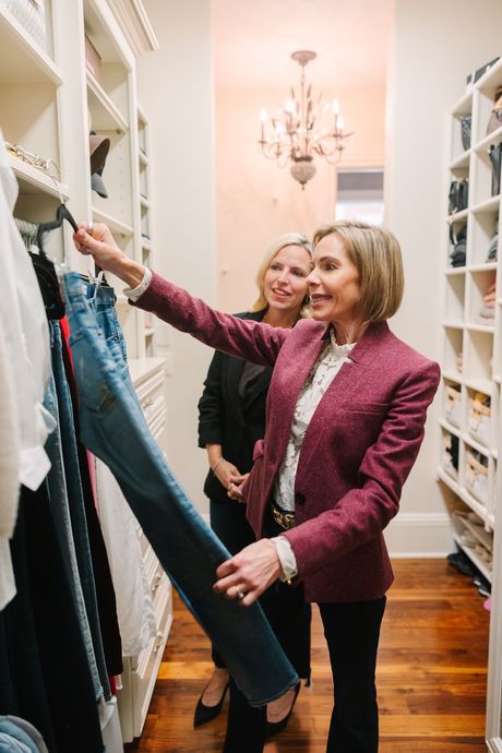Two women are standing in a walk in closet looking at clothes.