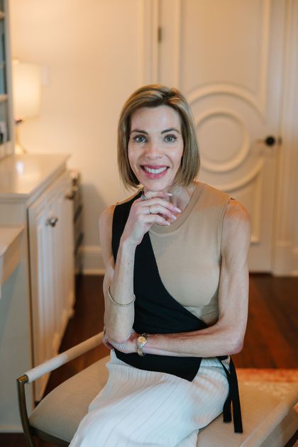 A woman is sitting in a chair with her hand on her chin and smiling.