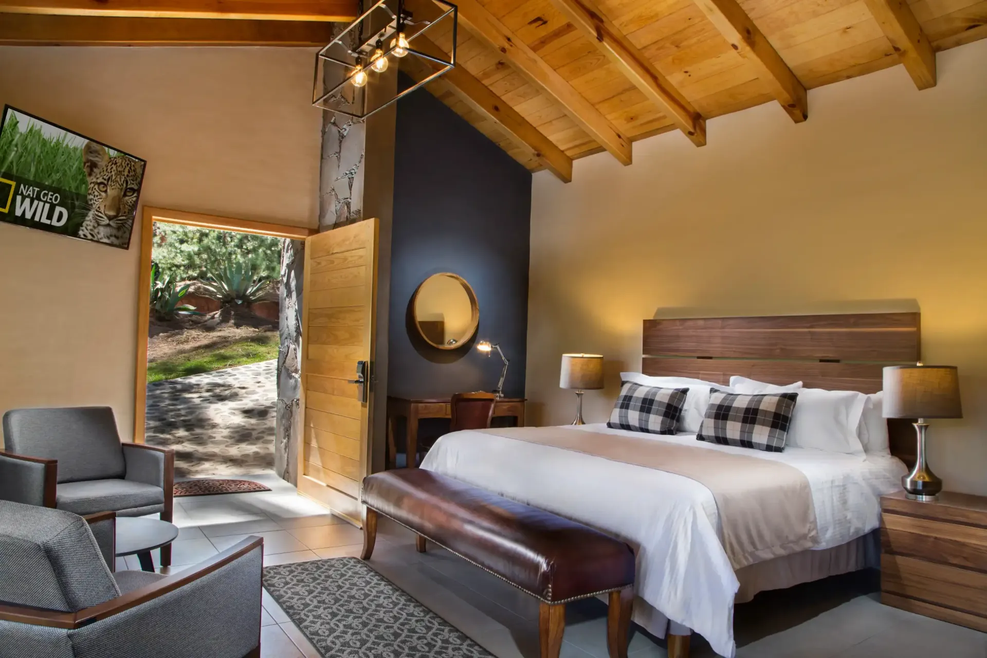 Un dormitorio con una cama king size, banco, silla y televisión.