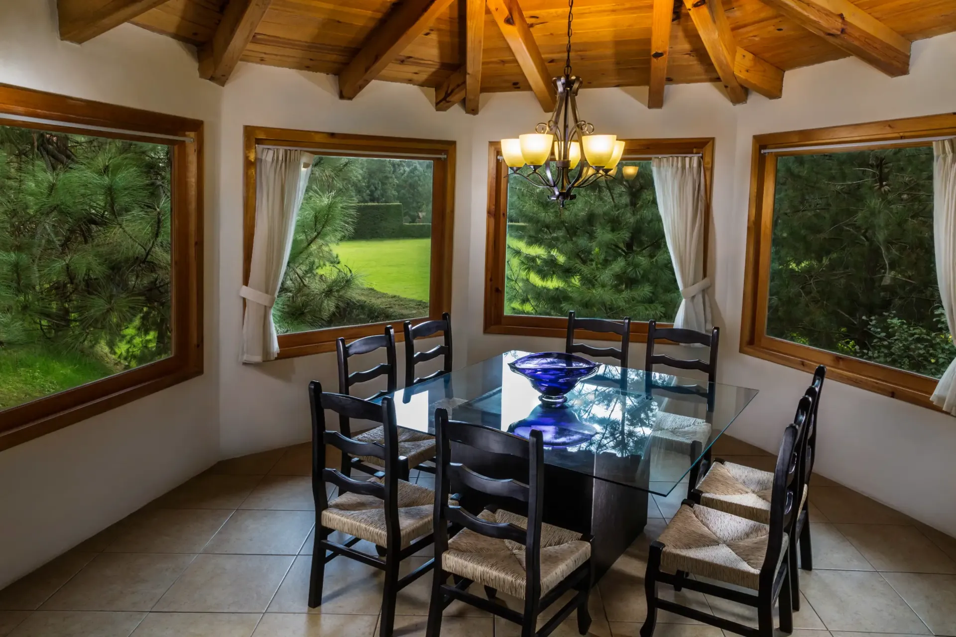 Un comedor con mesa y sillas y muchas ventanas.
