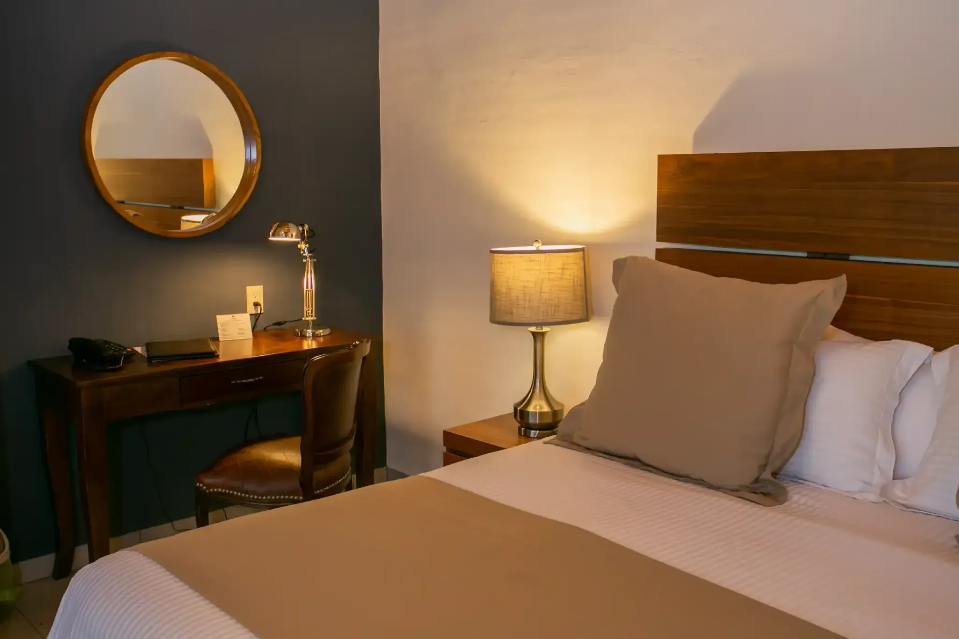 Un dormitorio con cama, escritorio, lámpara y espejo.