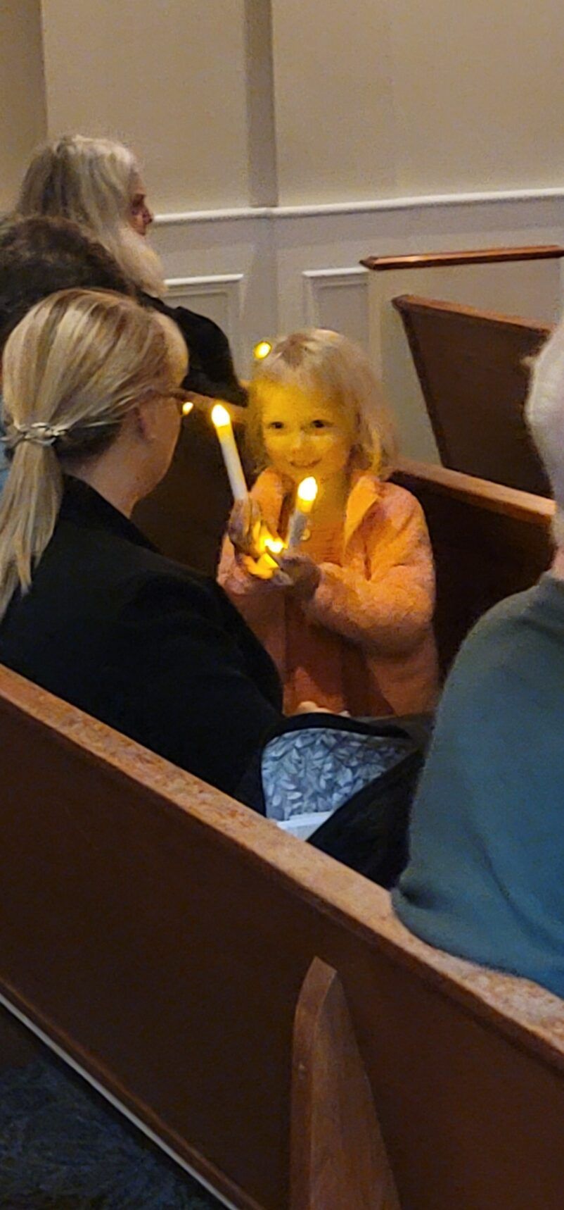 Young child holding a glowing candle in a church pew during a service