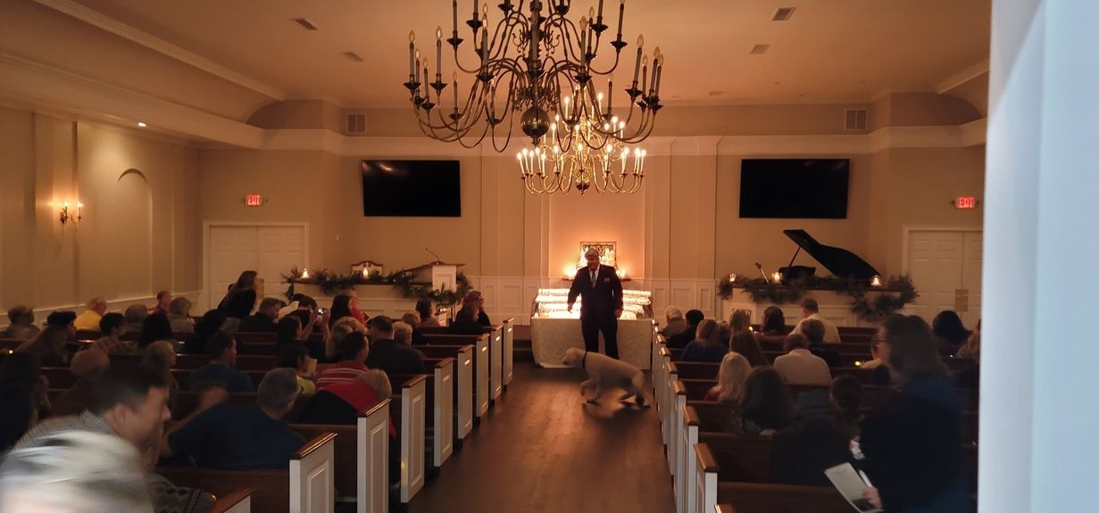 Audience seated in a church hall facing a speaker at a podium under a chandelier