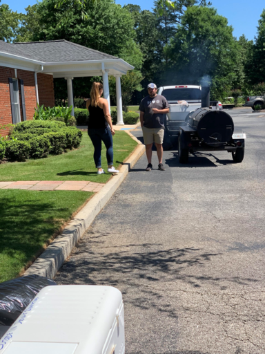Two people stand by a smoking black vehicle on a suburban street near a house.