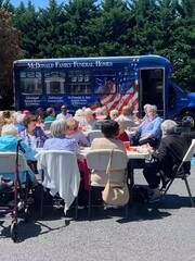 People seated outdoors facing a blue food truck at an American flag-themed community event
