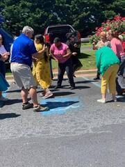 People dancing in a parking lot around a blue ground marking on a sunny day