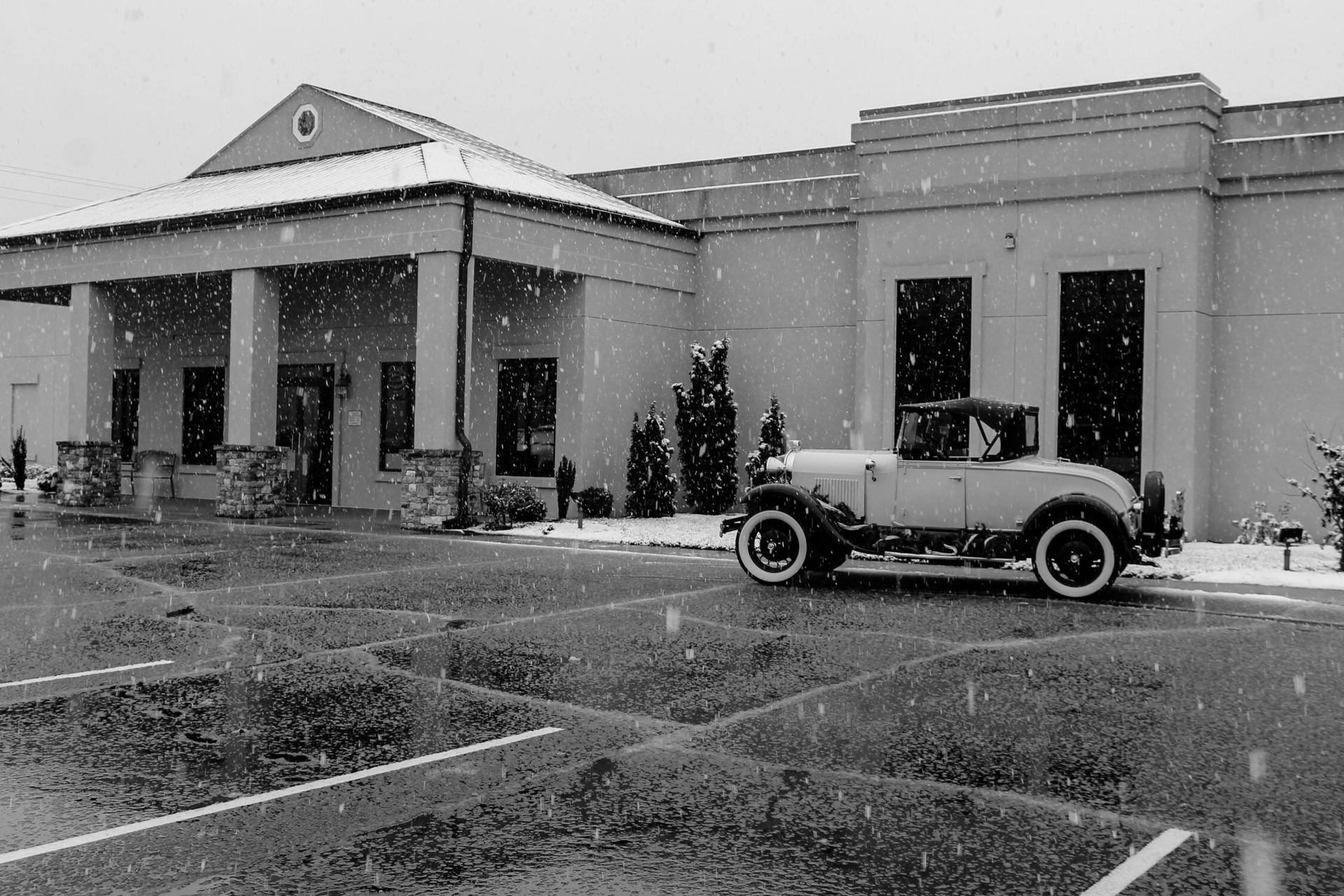 Snowy scene of a building entrance with a vintage car parked outside.