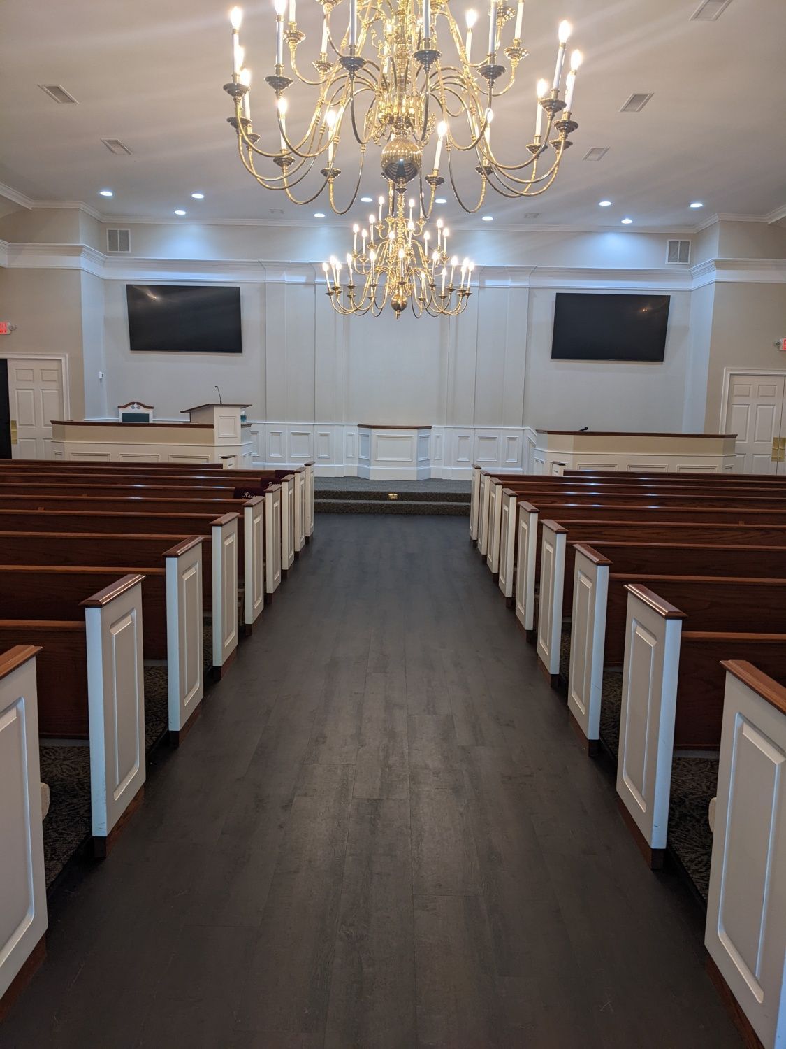 Empty church sanctuary with wooden pews, chandeliers, and a center aisle leading to the altar