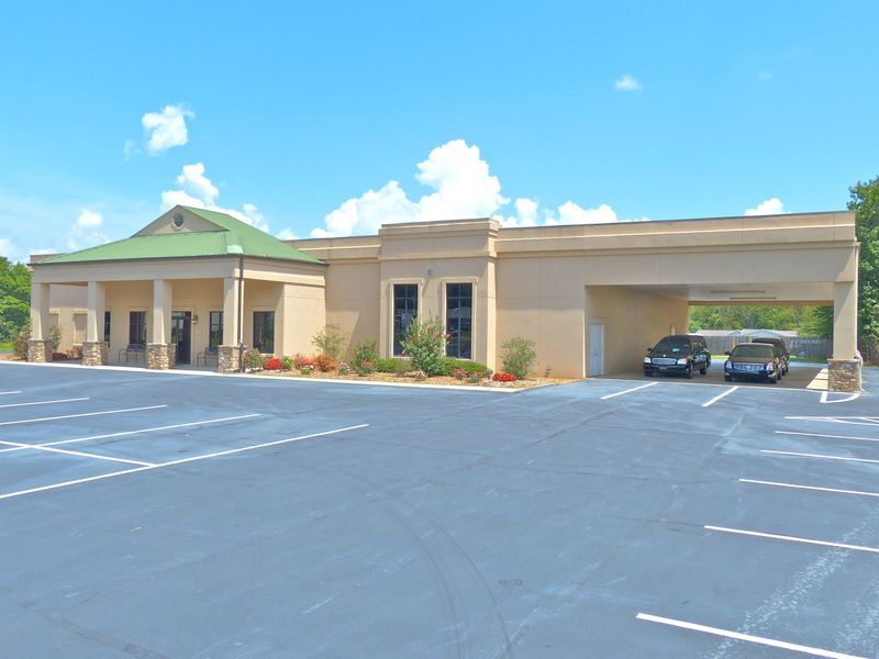 Single-story beige building with green roof and parking lot under a blue sky