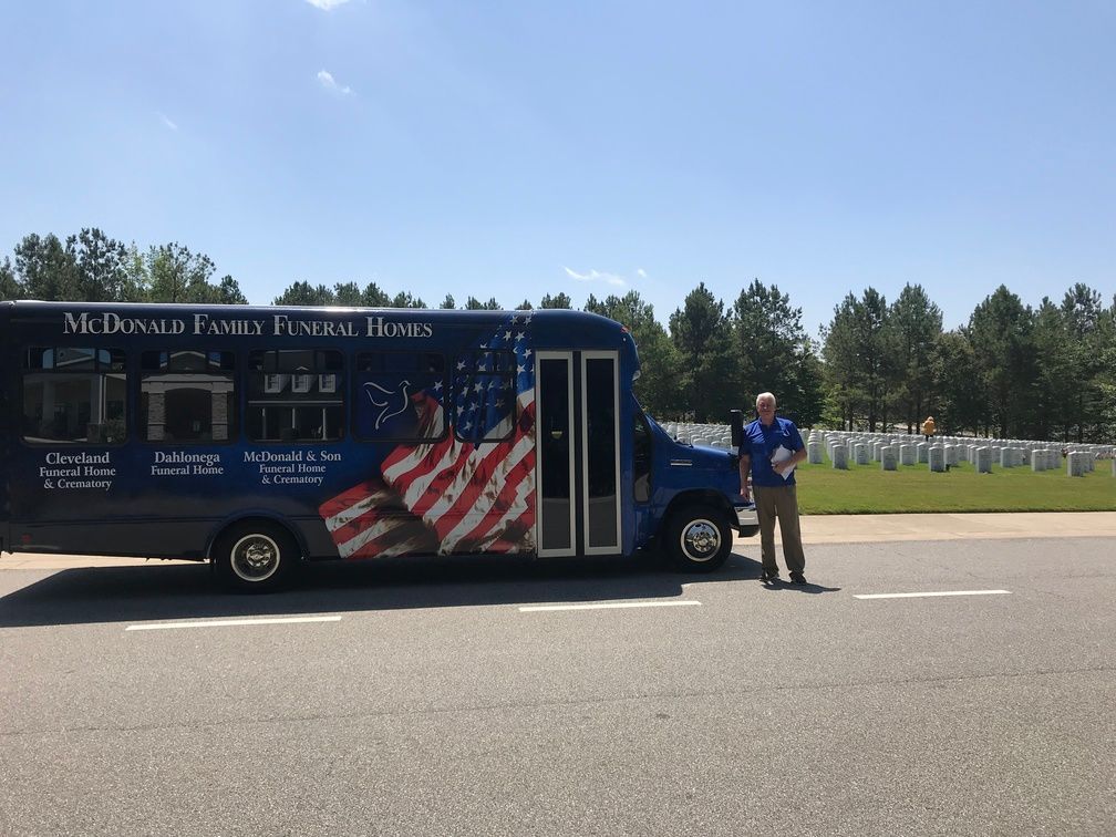 Mobile funeral home bus with U.S. flag design parked on roadside beside a standing person