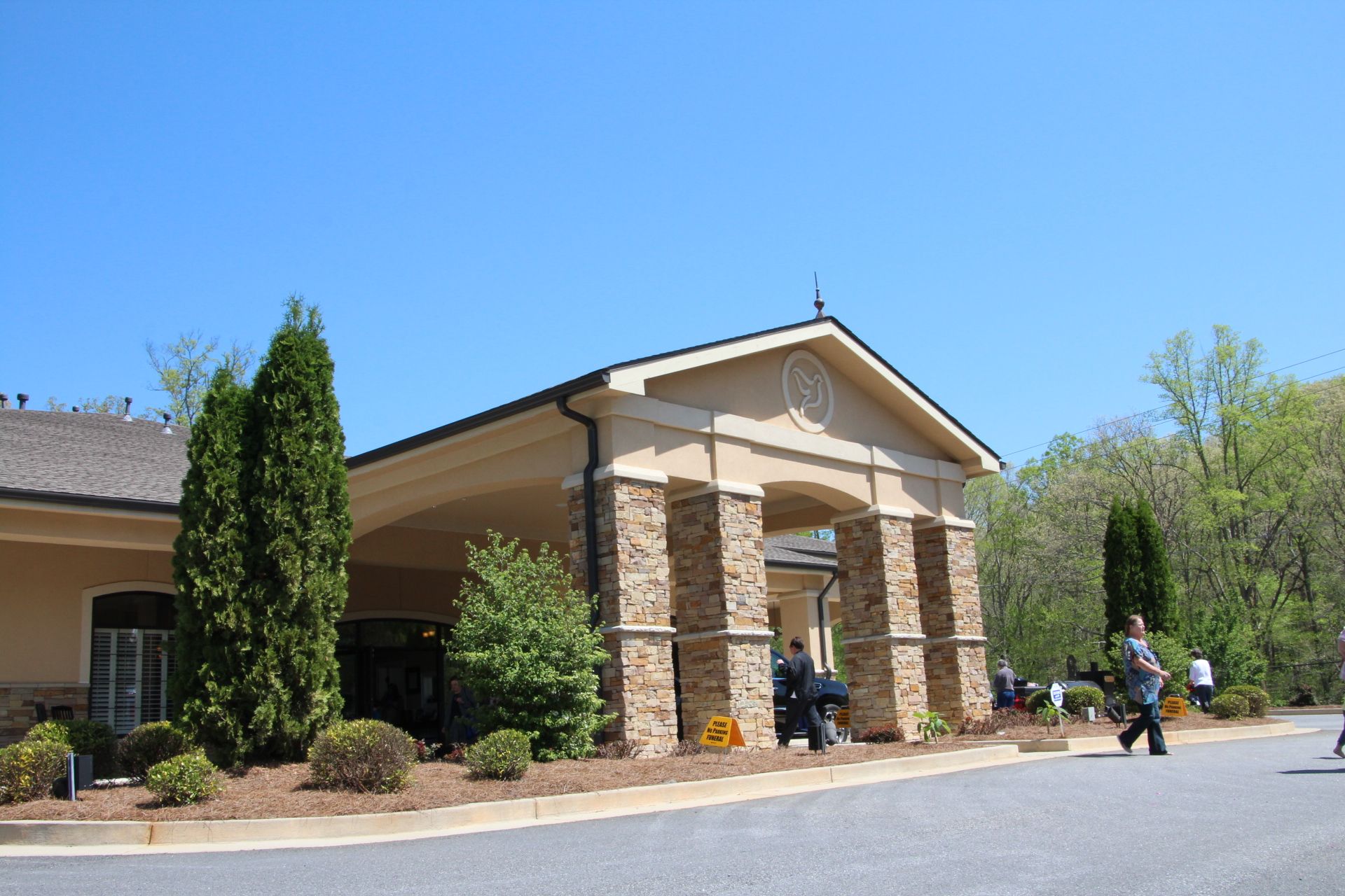 Brick building entrance with columns and a few people outside on a sunny day