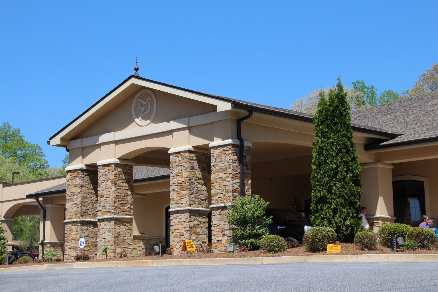 Stone-pillared building entrance with peaked roof and landscaping under a clear blue sky