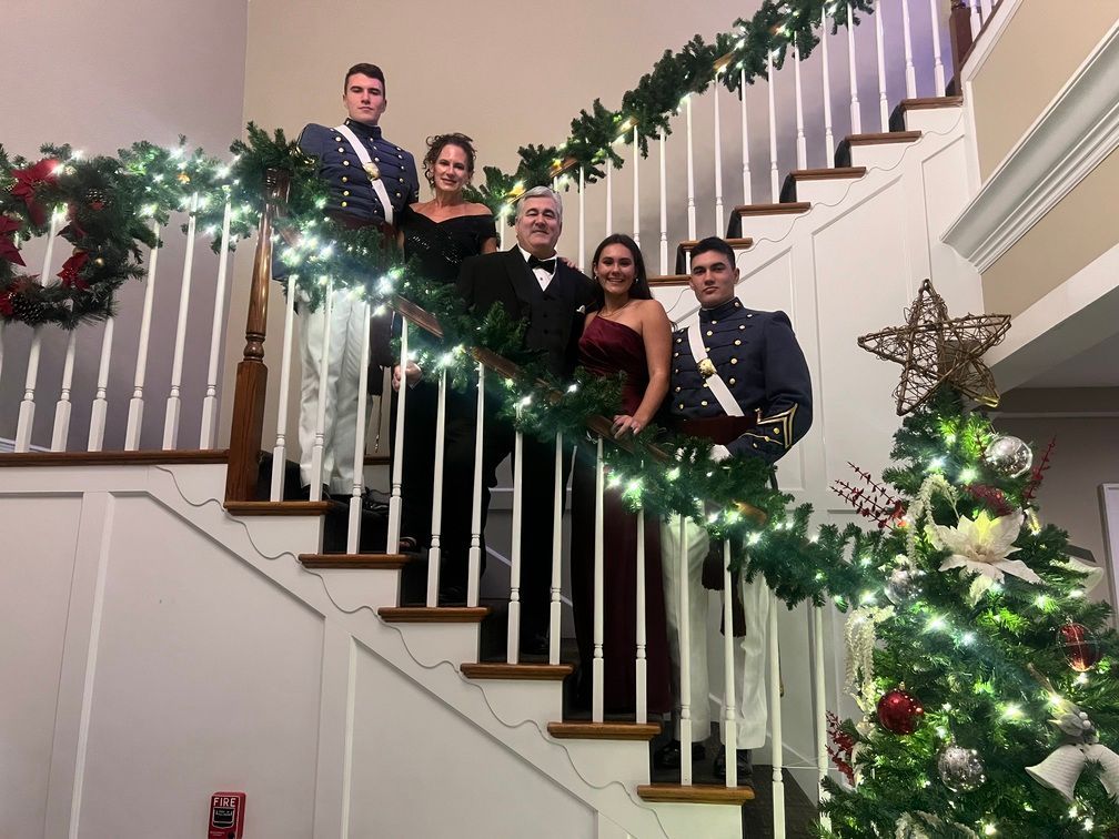 Five people posing on a staircase decorated with holiday garland and lights