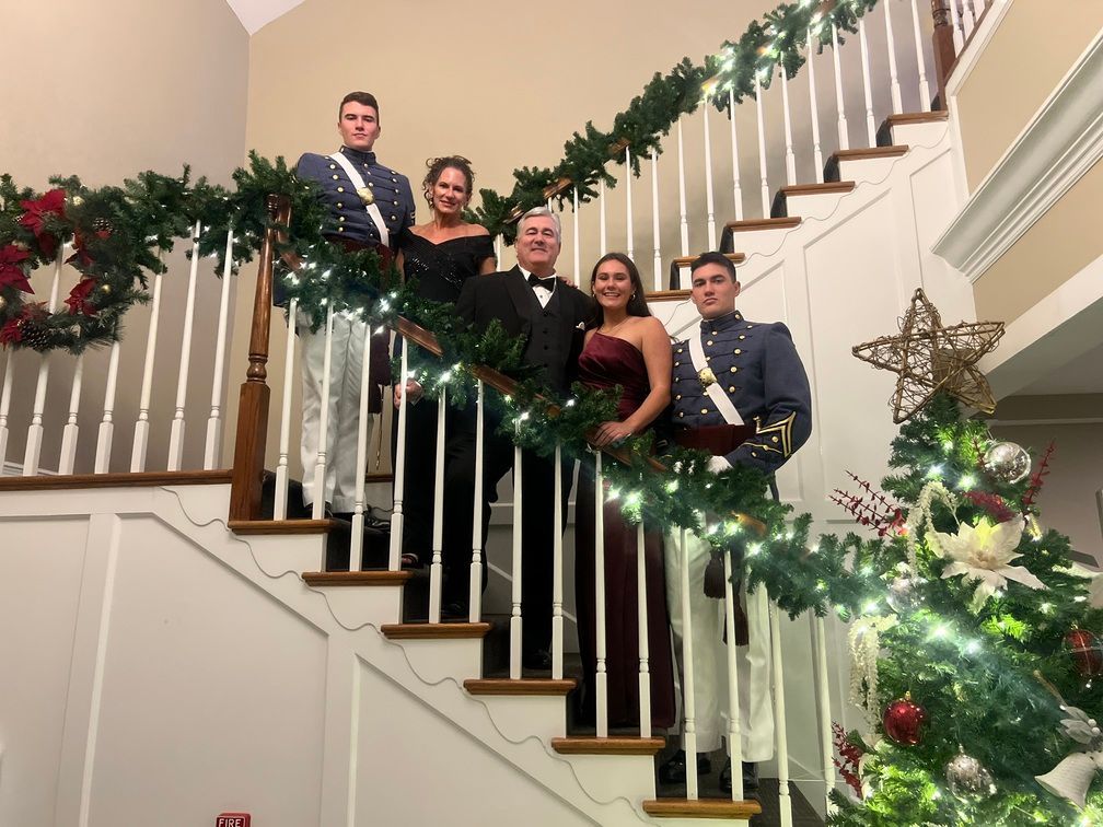 Four people posing on a decorated indoor staircase with holiday garland and lights