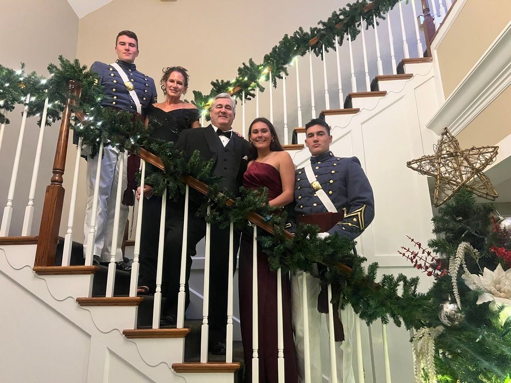 Five people posing on a decorated staircase with holiday garland and Christmas decor