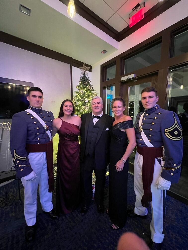 Five people in formal attire standing together at an indoor event, with two in military dress uniforms.
