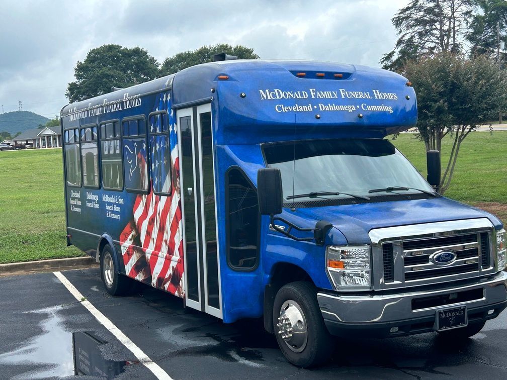 Blue shuttle bus with patriotic decals parked on a wet roadway near a grassy field