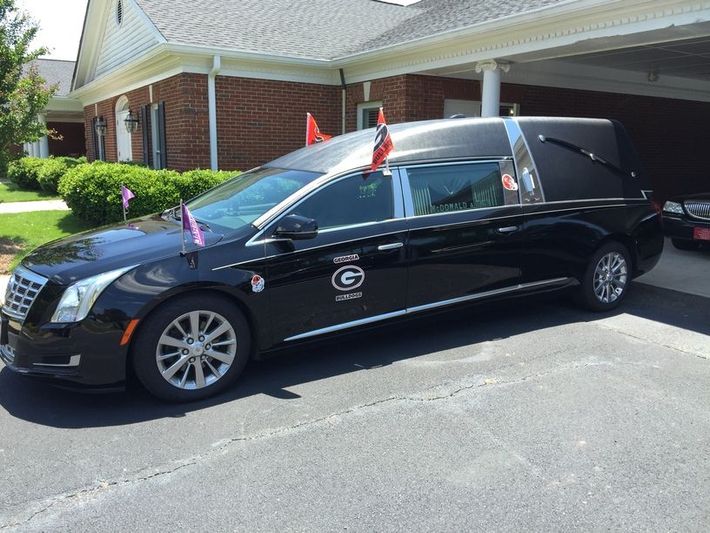 Black hearse parked outside a brick building, decorated with small flags on the roof.