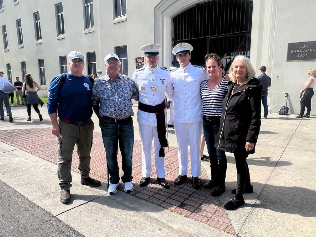 Five people pose outdoors in front of a building, with two in white uniforms and others in casual clothes.