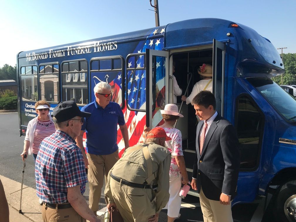 People boarding a blue bus with an American flag design, guided by a man in a suit.