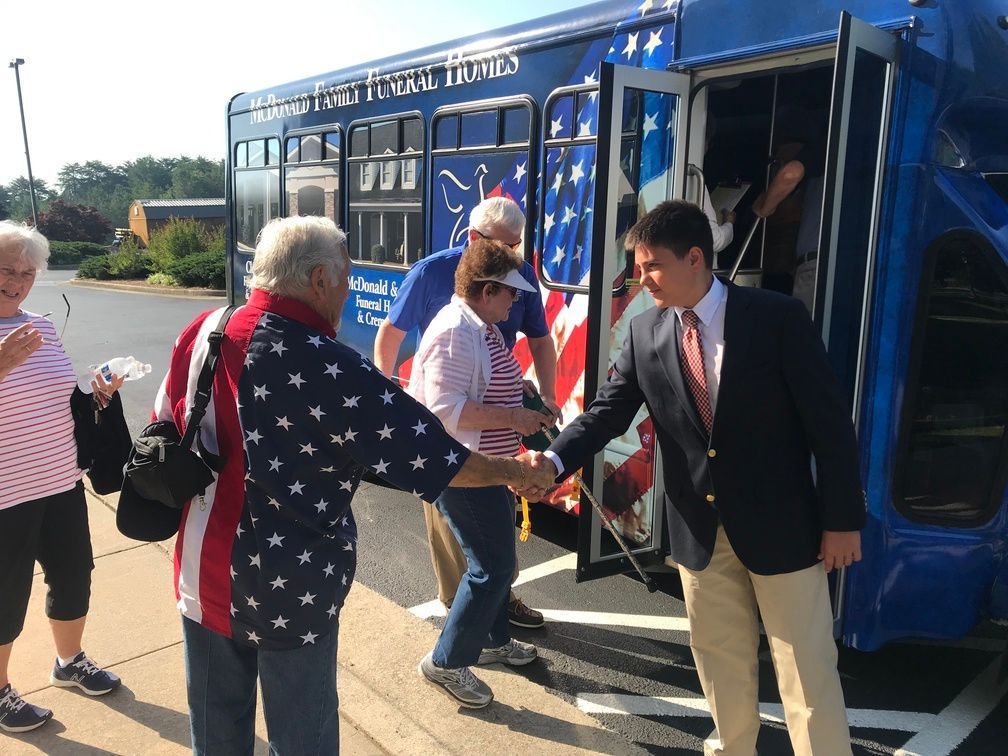People boarding a blue shuttle bus as a man in a suit assists them at the door.